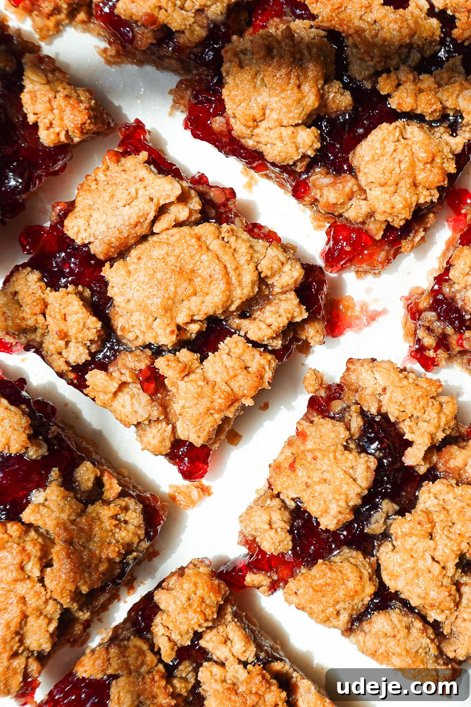 Healthy peanut butter and jelly bars sliced on parchment paper with jam oozing out