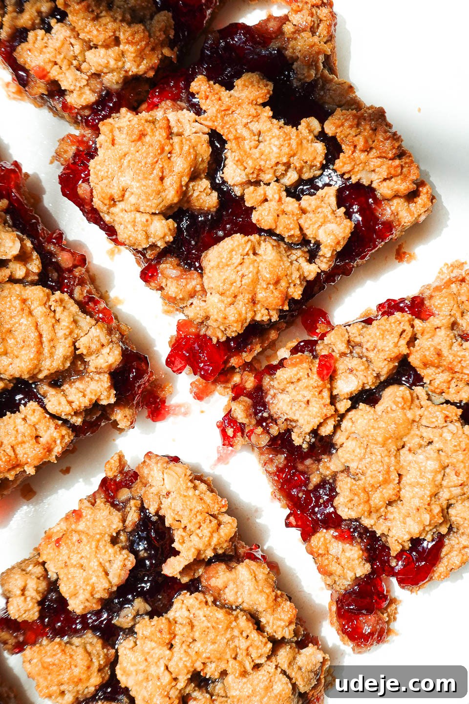 overhead shot of healthy peanut butter and jelly bars sliced on parchment paper with jam oozing out