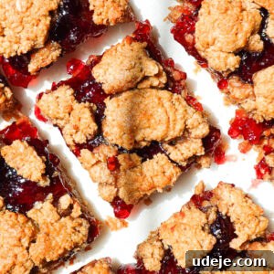 overhead shot of healthy peanut butter and jelly bars sliced on parchment paper with jam oozing out