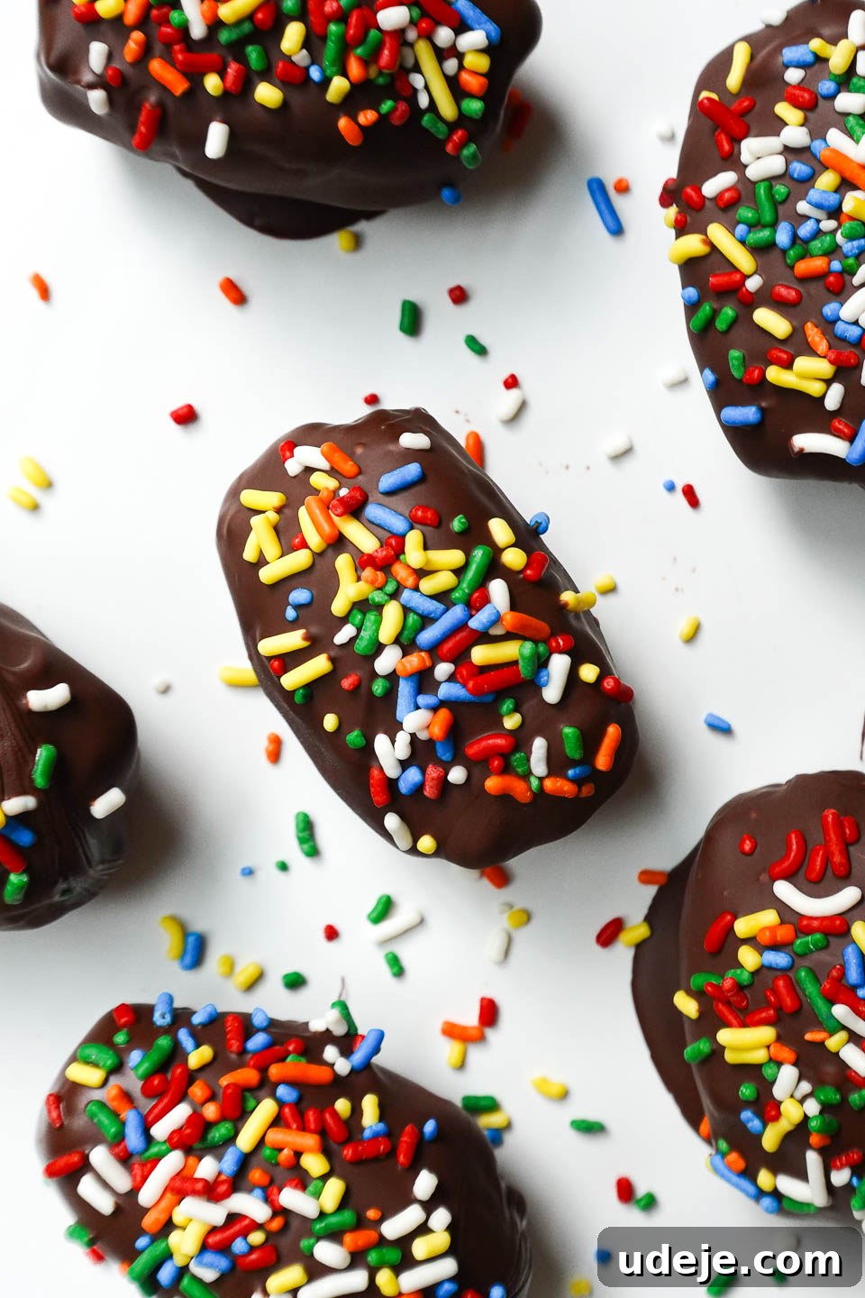 Stardust Brownie Dates 6 Cosmic brownie stuffed dates arranged on a white plate with rainbow sprinkles scattered around for a festive display and easy serving.