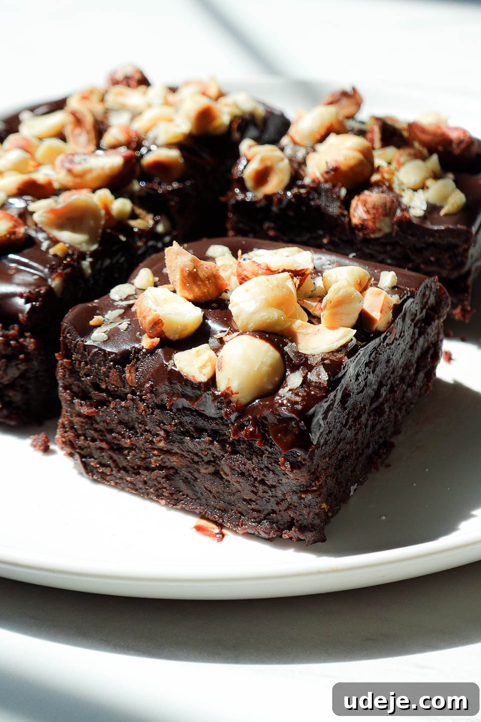 Side view of no bake vegan brownies with thick chocolate ganache layer and chopped hazelnuts on top