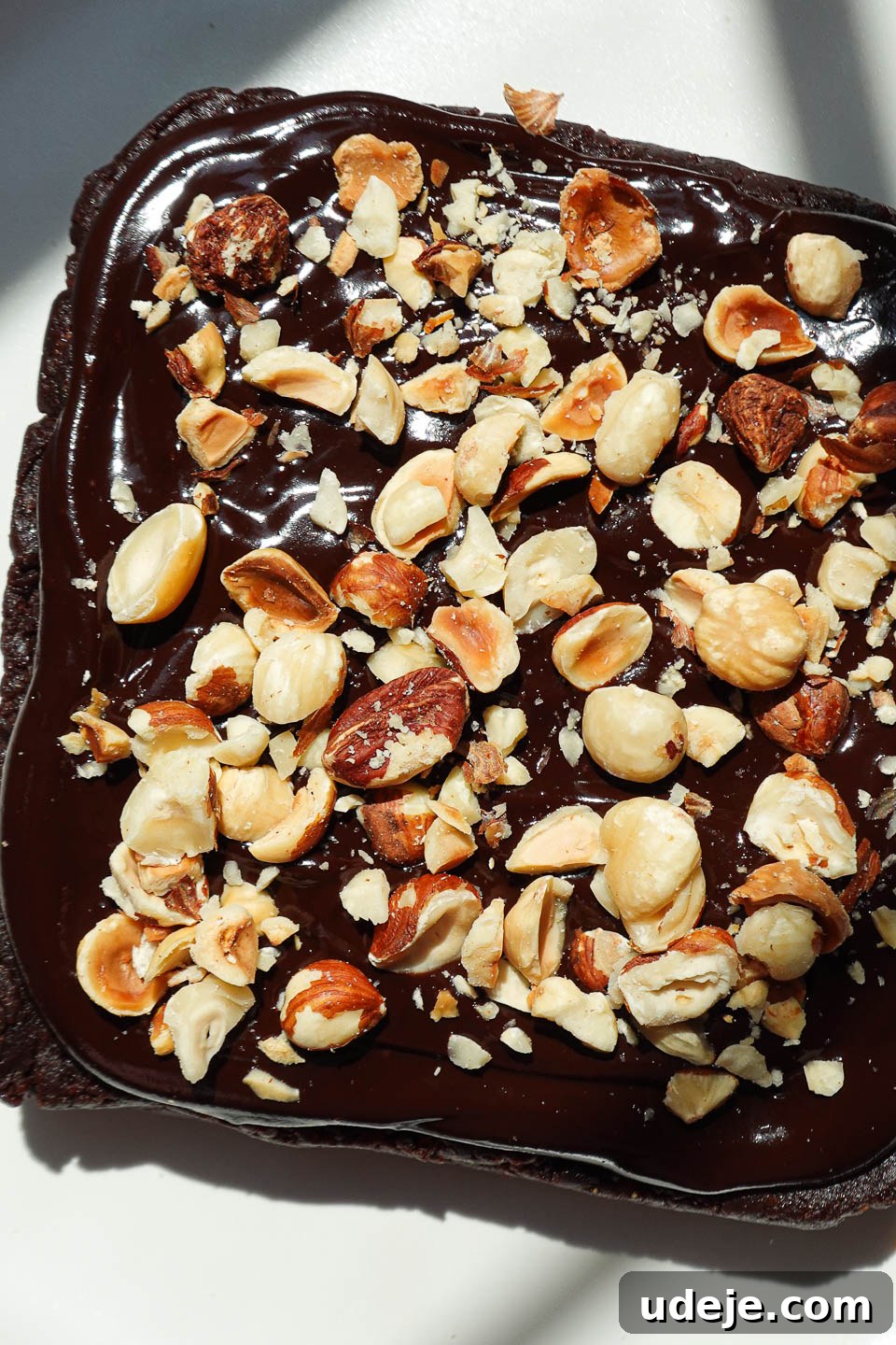 Overhead view of fudgy vegan brownies topped with silky chocolate ganache and chopped hazelnuts