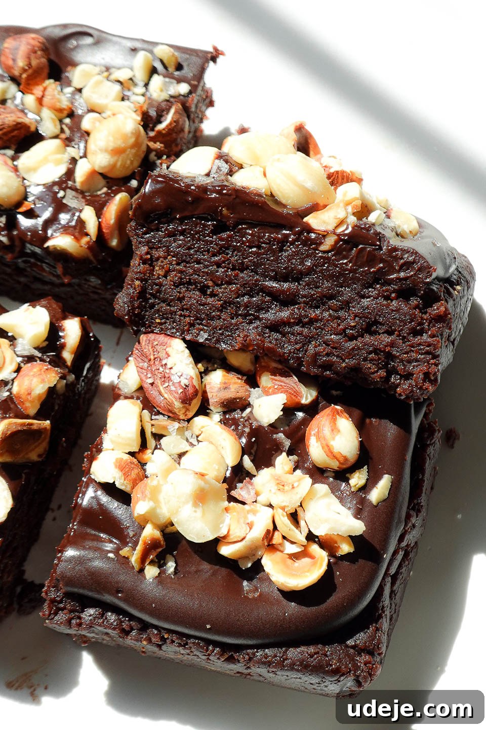 Close-up of fudgy, no-bake, healthy brownies topped with chocolate ganache and crunchy hazelnuts