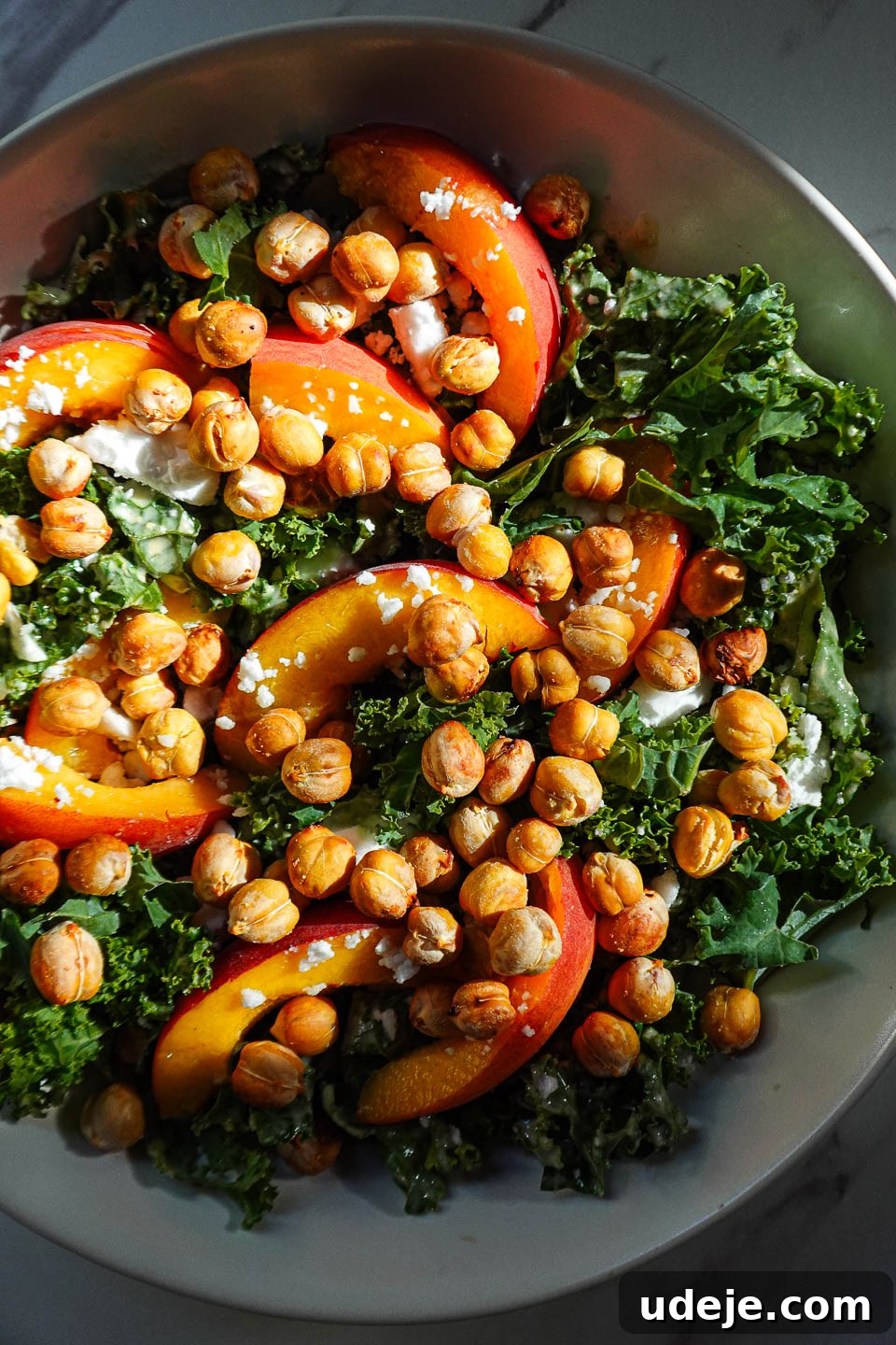 Bowl of kale salad with peaches, crispy chickpeas, vegan feta, and honey tahini dressing
