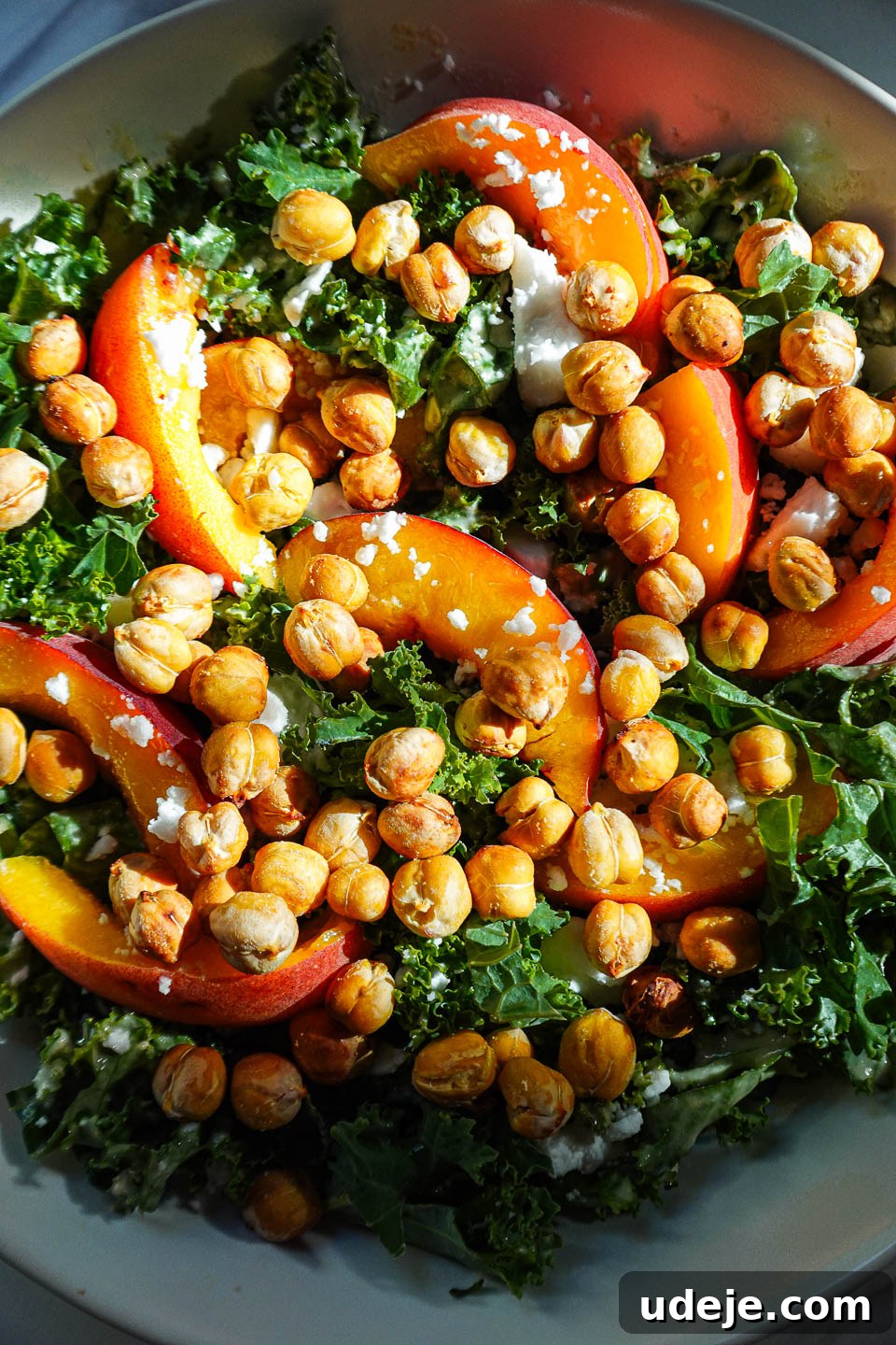 Close-up of peach kale salad topped with crispy chickpeas, vegan feta, fresh peaches, and a creamy tahini dressing