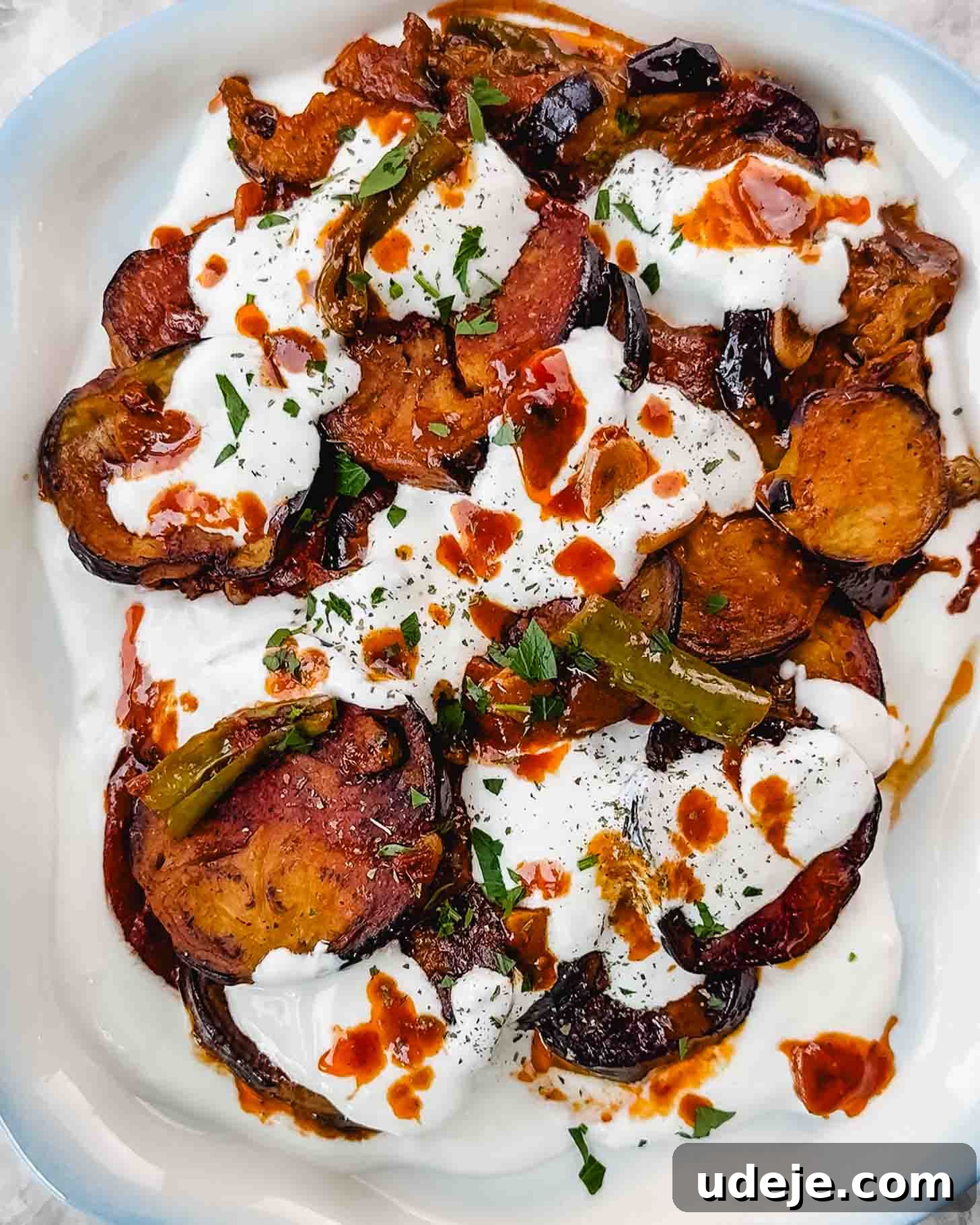 Borani Banjan Creamy Afghan Eggplant Yogurt Dip 12 A vibrant plate of Borani Banjan captures attention with its artful presentation. Golden-fried eggplant slices are generously crowned with a creamy white yogurt sauce, a rich red tomato sauce, bright green peppers, and a sprinkle of freshly chopped parsley, creating a visually appealing and flavorful Afghan delicacy.