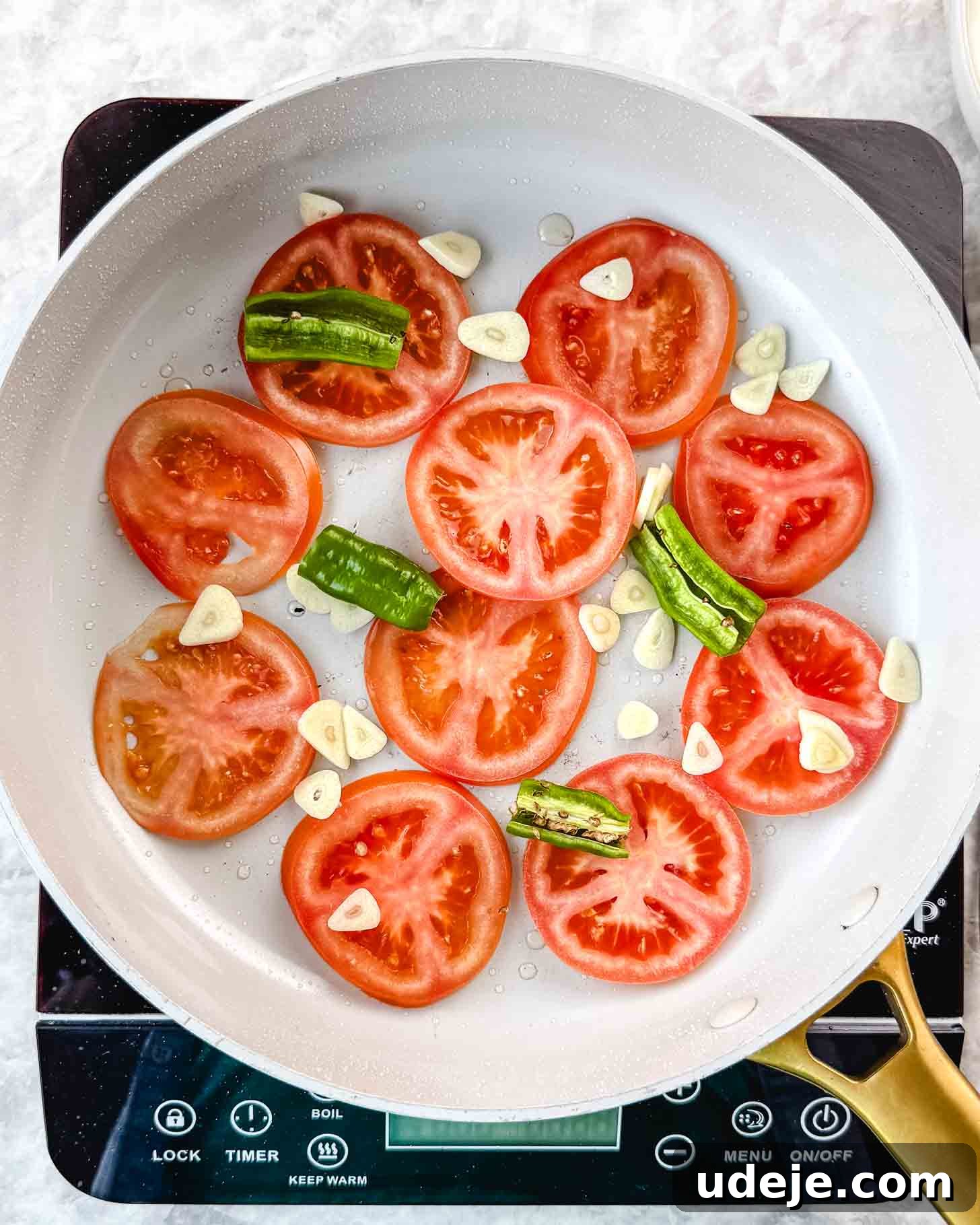 Borani Banjan Creamy Afghan Eggplant Yogurt Dip 8 Sliced ripe tomatoes, bright green chili peppers, and fragrant garlic pieces are carefully arranged in a pristine white frying pan, ready for cooking on an electric cooktop. This preparation forms a flavorful base for dishes such as Borani Banjan.