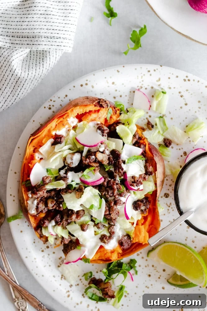 Aromatic Middle Eastern Stuffed Sweet Potatoes 2 Sweet potato stuffed with warmly spiced ground beef and topped with fresh vegetables and a creamy garlic yogurt tahini sauce, presented on a speckled plate.