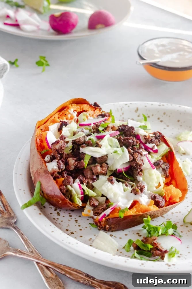 Aromatic Middle Eastern Stuffed Sweet Potatoes 3 Close-up of a perfectly baked sweet potato generously stuffed with spiced ground beef, topped with vibrant fresh vegetables and a drizzle of creamy garlic yogurt tahini sauce on a speckled ceramic plate.