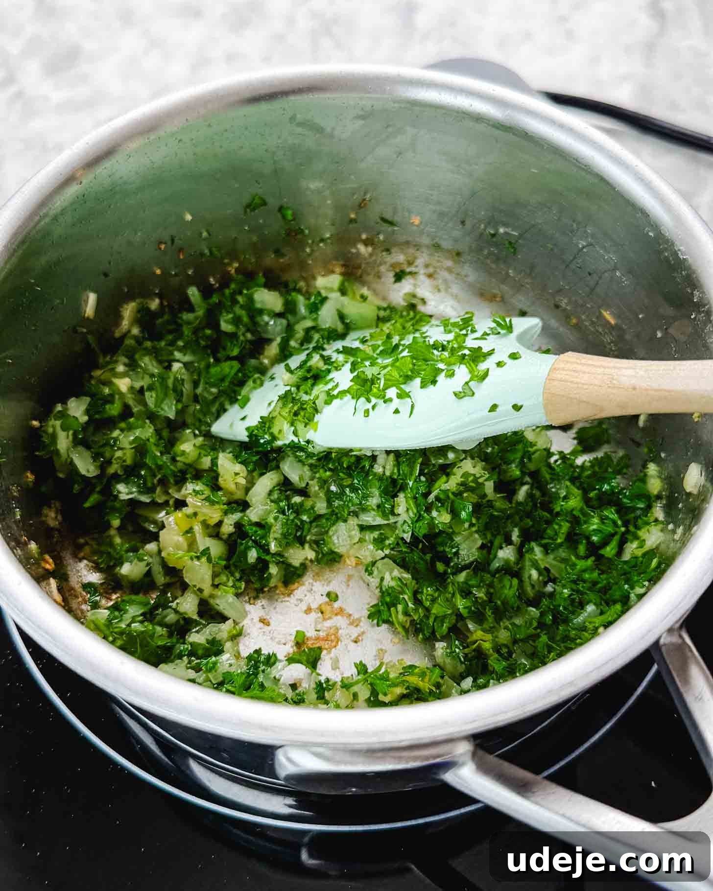 Samke Harra: Lebanon's Signature Spicy Fish 6 A metal pot with chopped parsley and chopped onions softening with a light blue spatula.