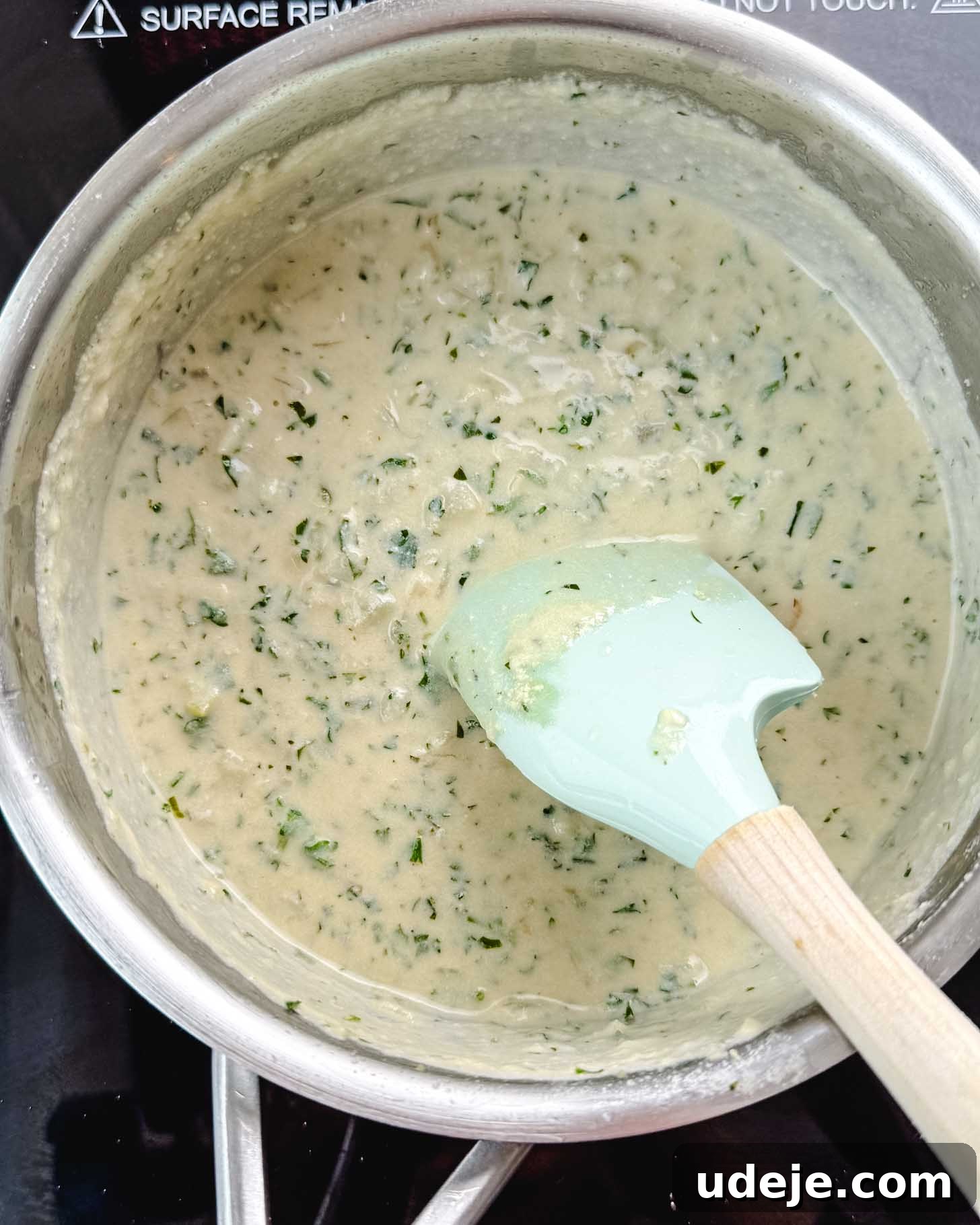 Samke Harra: Lebanon's Signature Spicy Fish 7 Metal pot with a white creamy sauce with specks of chopped cilantro and a light blue spatula with a wooden handle.