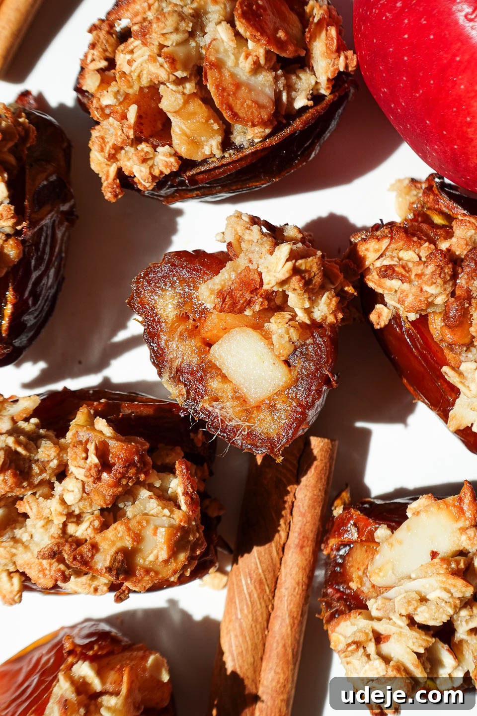 Golden Apple Crisp Date Bites 2 Bite taken out of an apple crisp stuffed date showing gooey date and cinnamon apple center, with a warm, inviting glow.