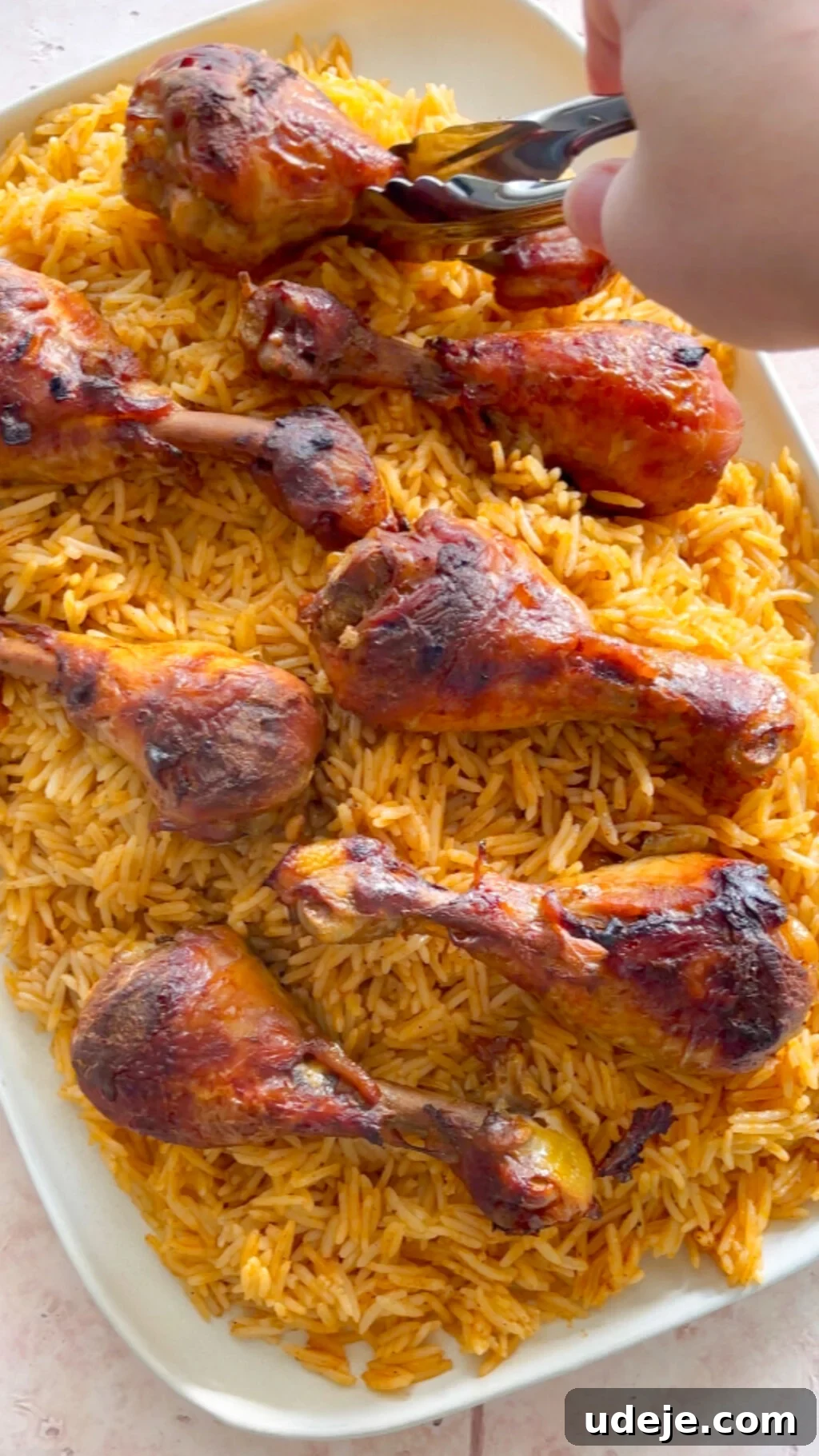 Machboos and Kabsa Aromatic Chicken and Rice 14 orange rice and browned cooked drumsticks being plated on a large rectangular platter.