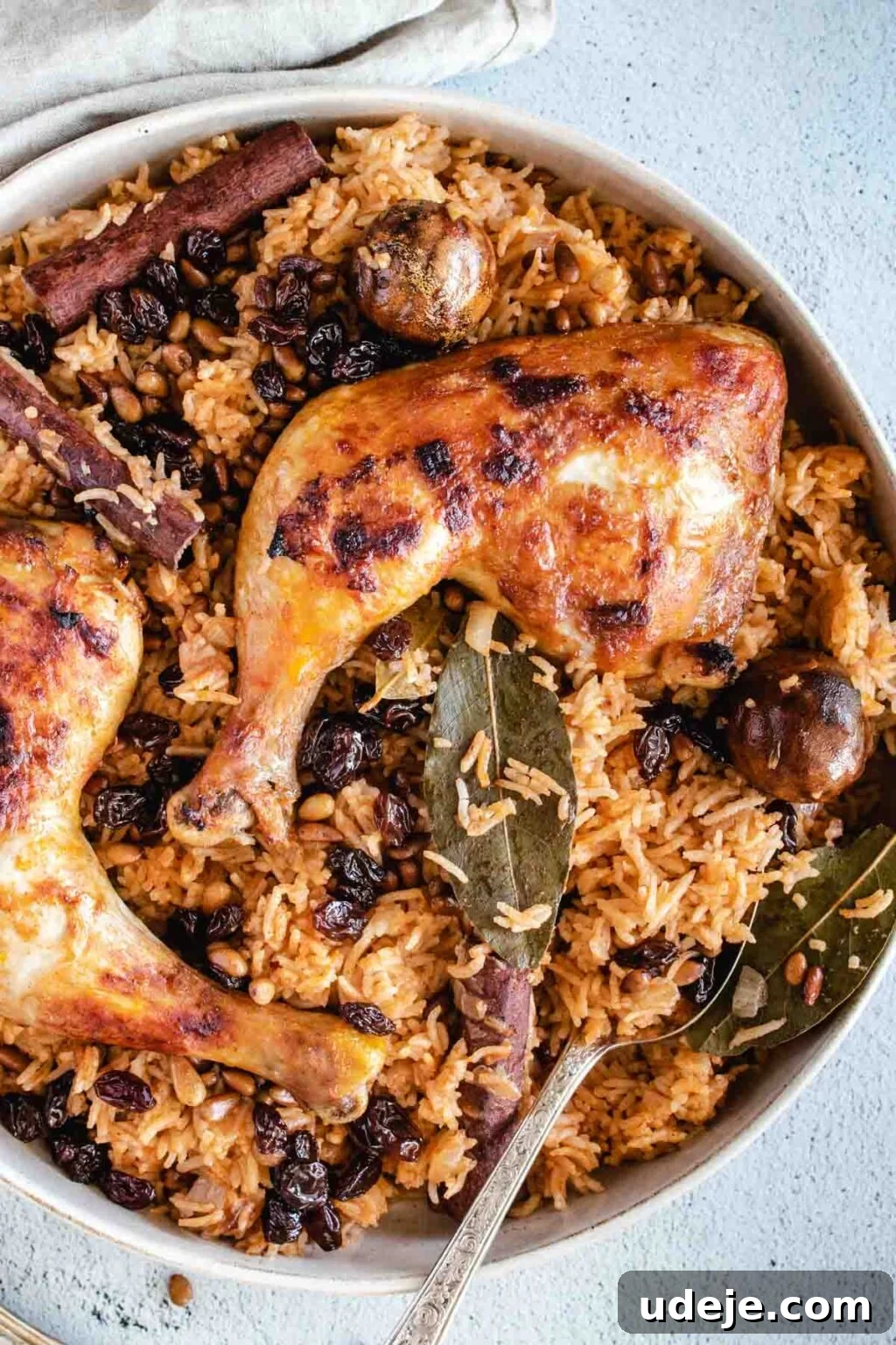 Machboos and Kabsa Aromatic Chicken and Rice 15 chicken kabsa which is red rice, with full crispy chicken legs on top, garnished with raisins and pine nuts, with whole spices bay leaves, dried lime and cinnamon sticks