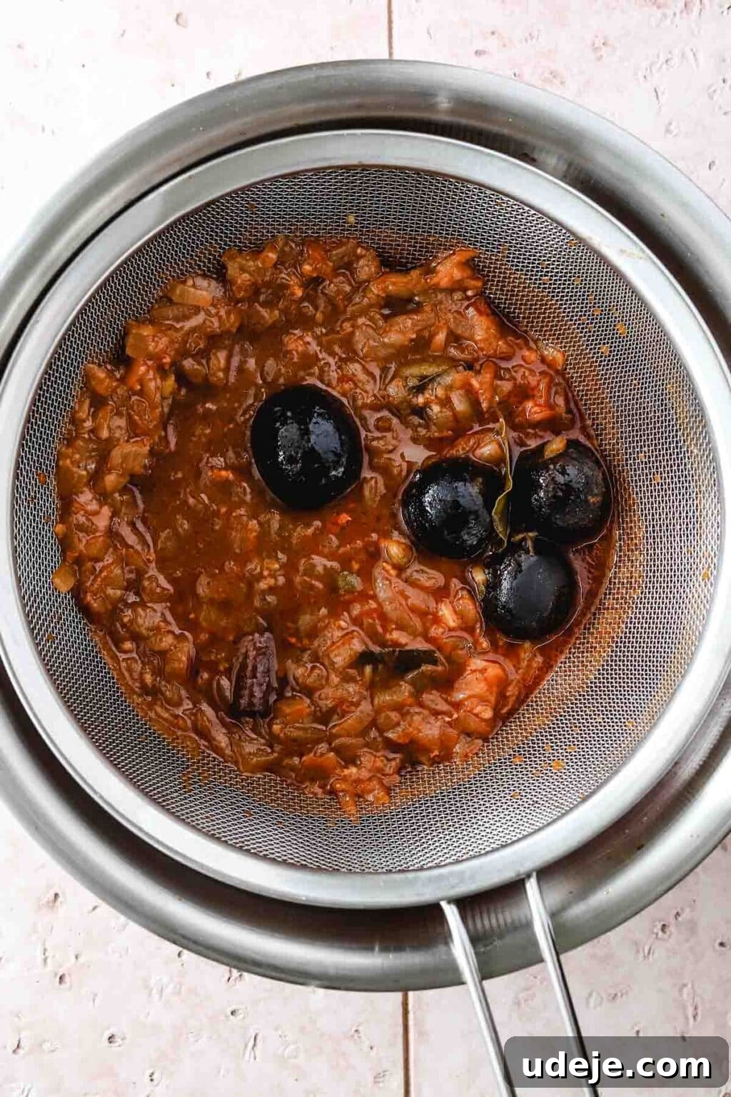 Machboos and Kabsa Aromatic Chicken and Rice 9 onions and dry limes in a strainer over a silver pot on a light coloured tiled background