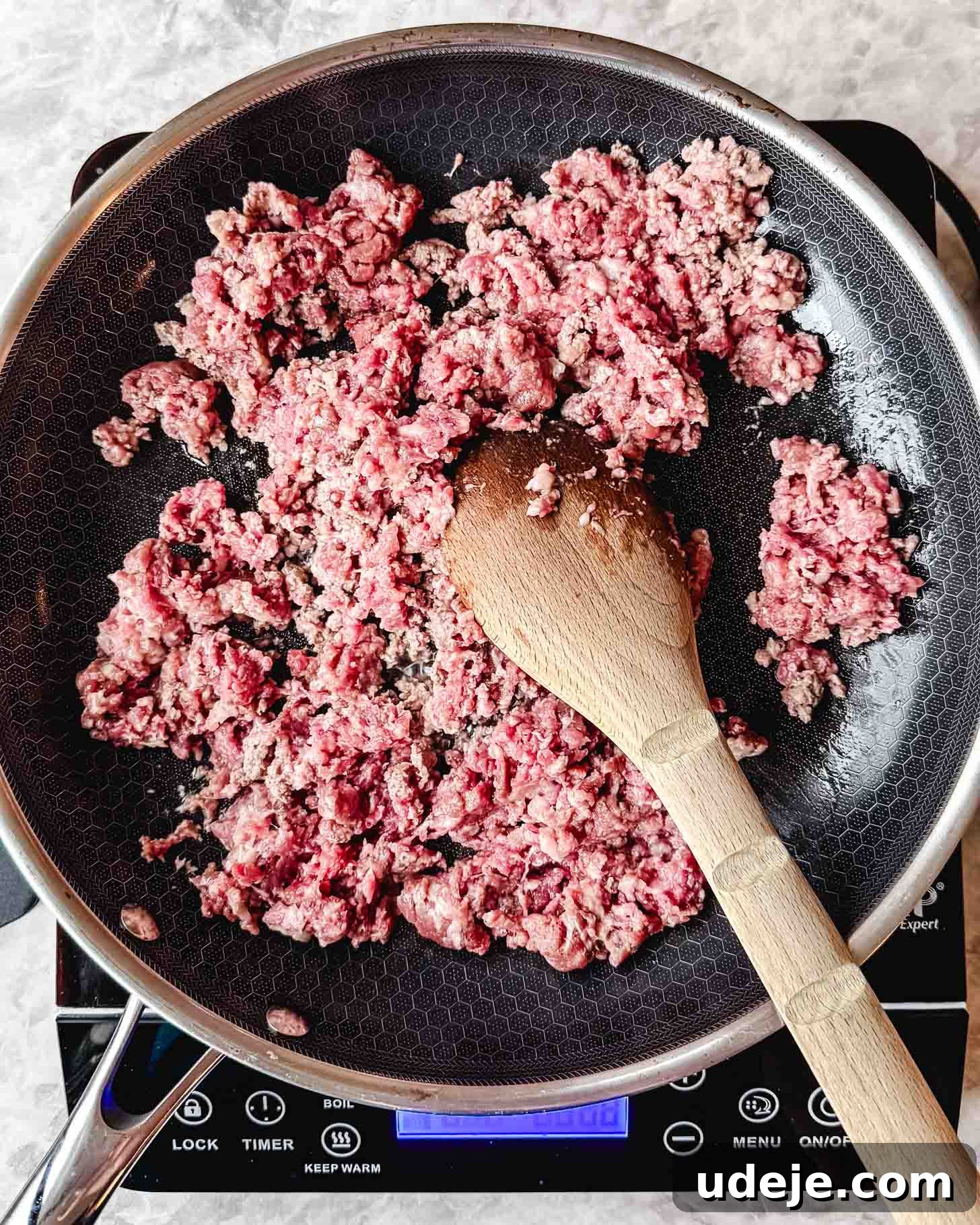 Easy Middle Eastern Spiced Beef Bowls 3 Raw pink ground beef being broken up with a wooden spoon in a dark frying pan on a marble countertop.