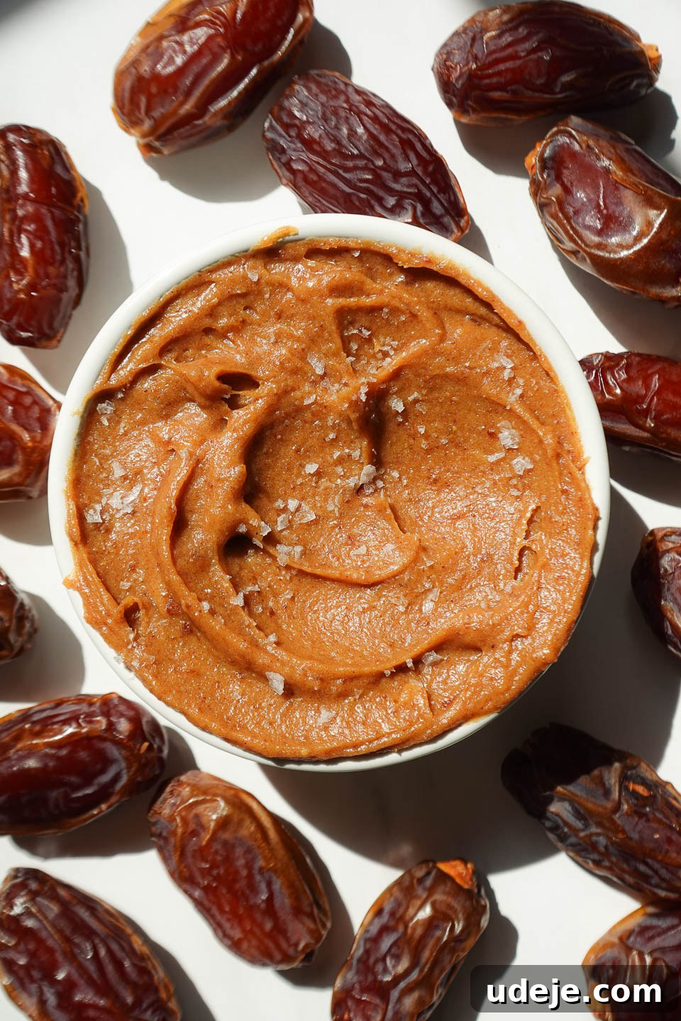 Golden Date Delight 2 Healthy date caramel in a bowl surrounded by fresh dates and topped with flaky sea salt.