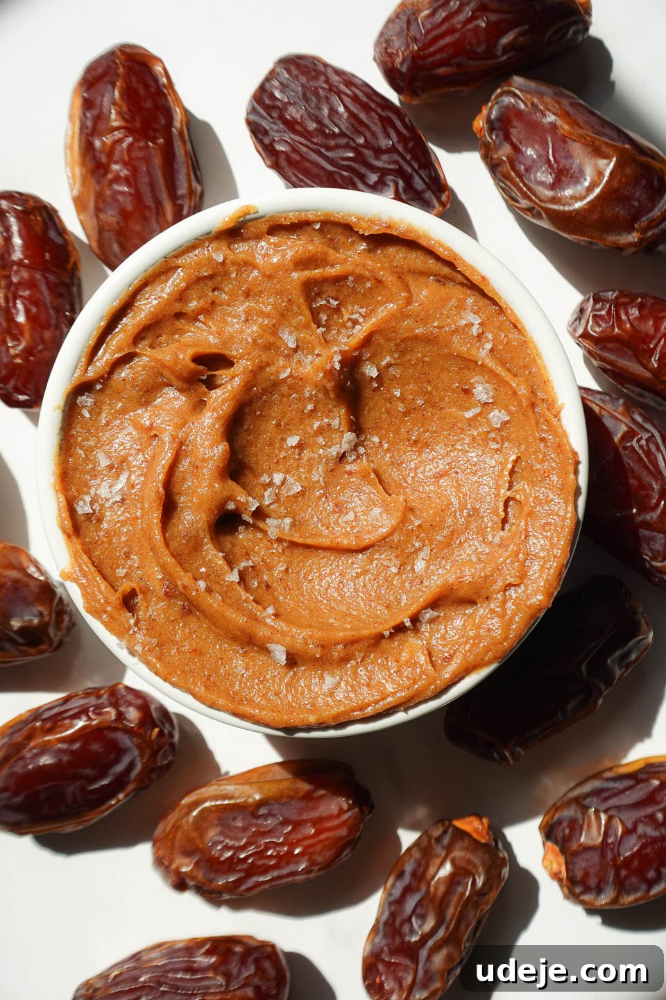 Golden Date Delight 4 Healthy date caramel in a bowl surrounded by fresh dates and topped with flaky sea salt.
