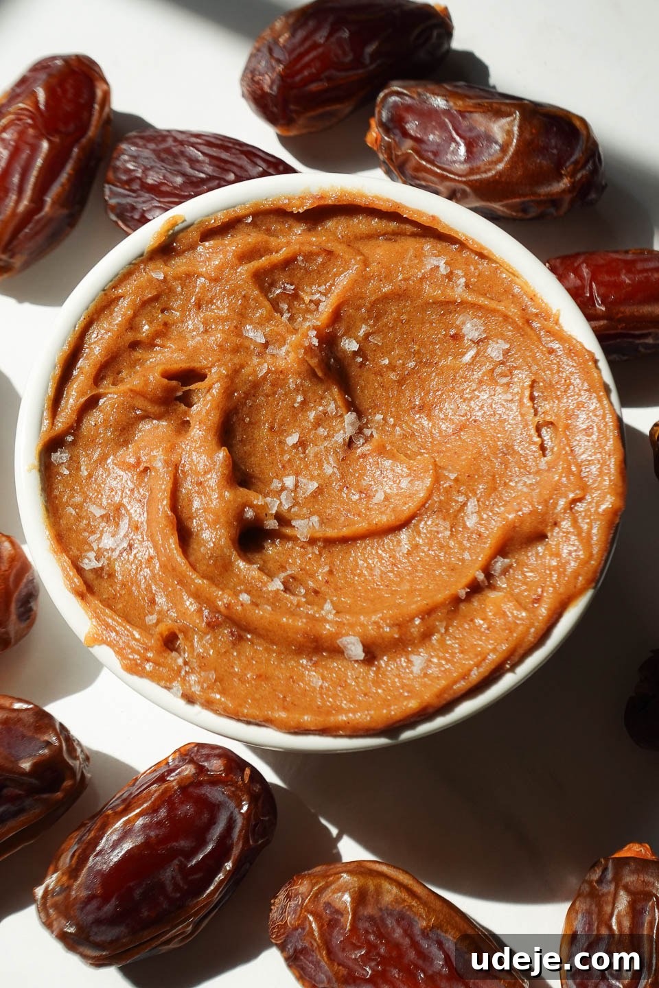 Golden Date Delight 5 Healthy date caramel in a bowl surrounded by fresh dates and topped with flaky sea salt.