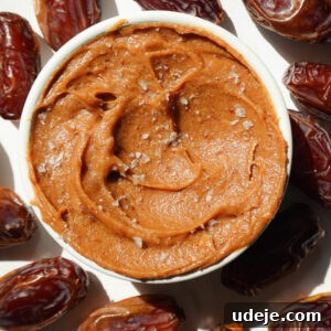 Healthy date caramel in a bowl surrounded by fresh dates and topped with flaky sea salt.