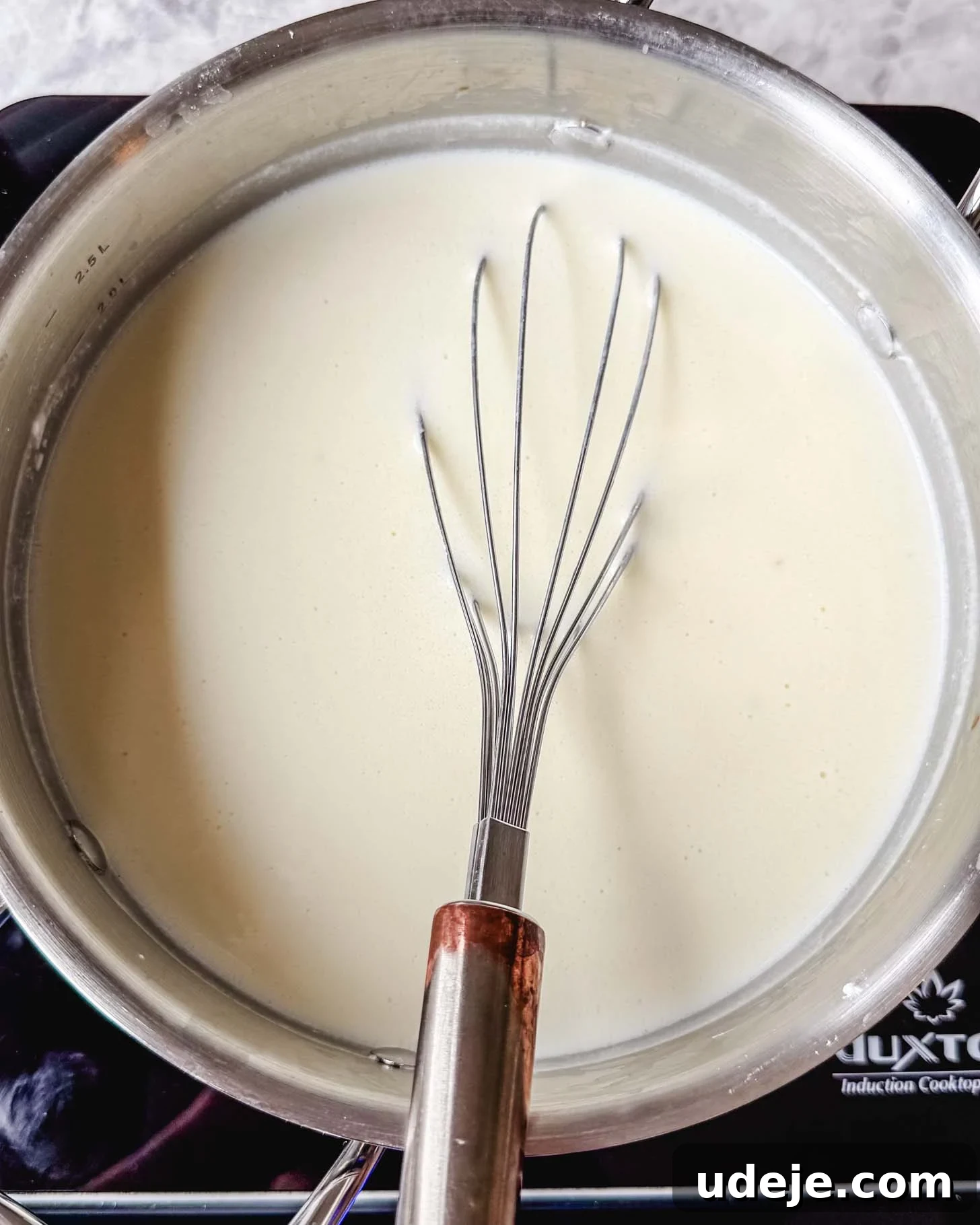 The Ultimate Meatball Soup with Yogurt and Pasta 5 Steel pot with a white creamy liquid with a metal whisk inside on a marble surface.