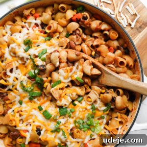 vegan chili mac and cheese made in one-pot and topped with melted vegan cheese and scallions with a wooden spoon