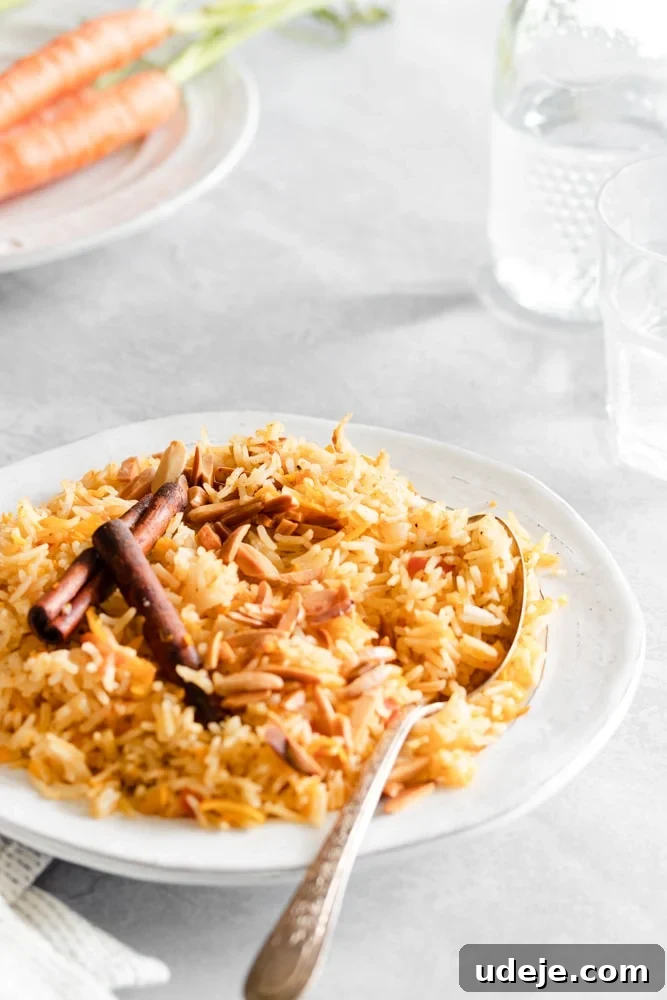 Authentic Iraqi Carrot Pilaf 3 Carrot rice served in a white plate, garnished with friend almonds and cinnamon sticks on a grey background