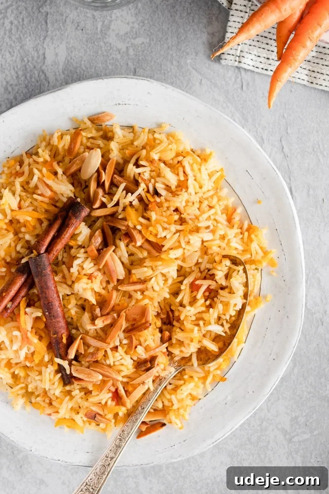 Authentic Iraqi Carrot Pilaf 5 Carrot rice served in a white plate, garnished with friend almonds and cinnamon sticks on a grey background