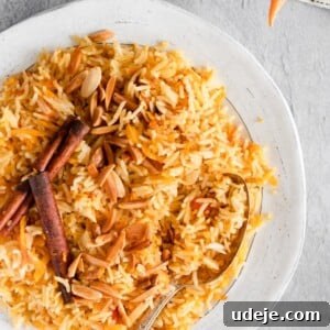 Carrot rice served in a white plate, garnished with fried almonds on a grey background