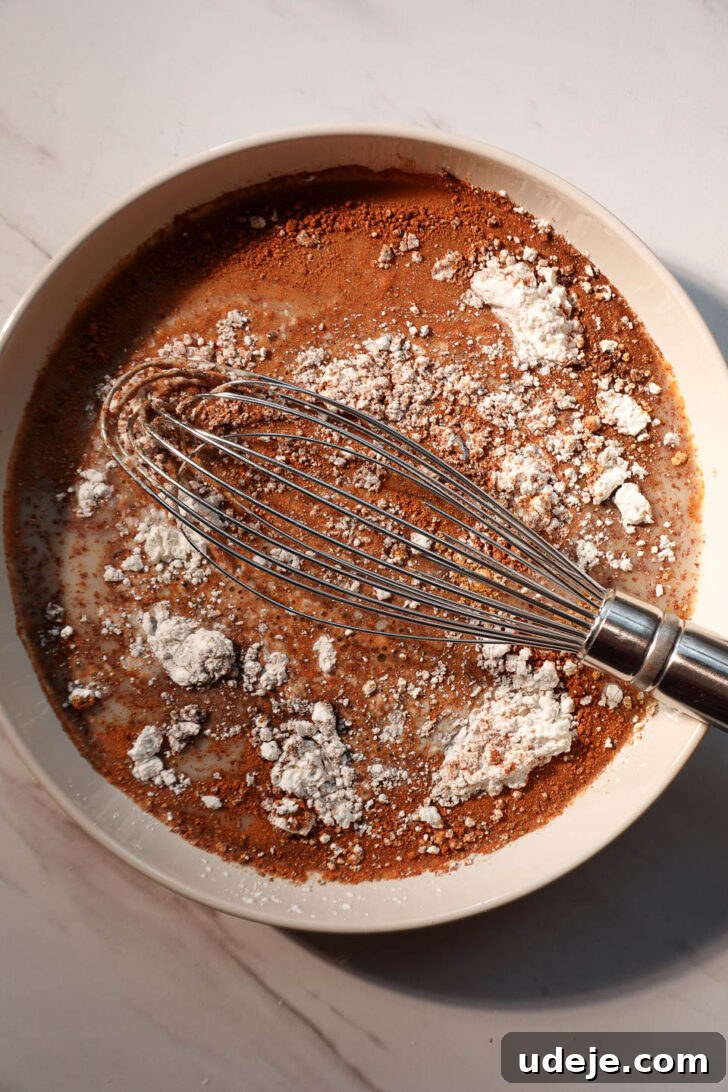Spiced Vegan Gingerbread French Toast 4 Close-up of a hand whisking vegan gingerbread French toast batter in a bowl, showing the creamy texture and spices