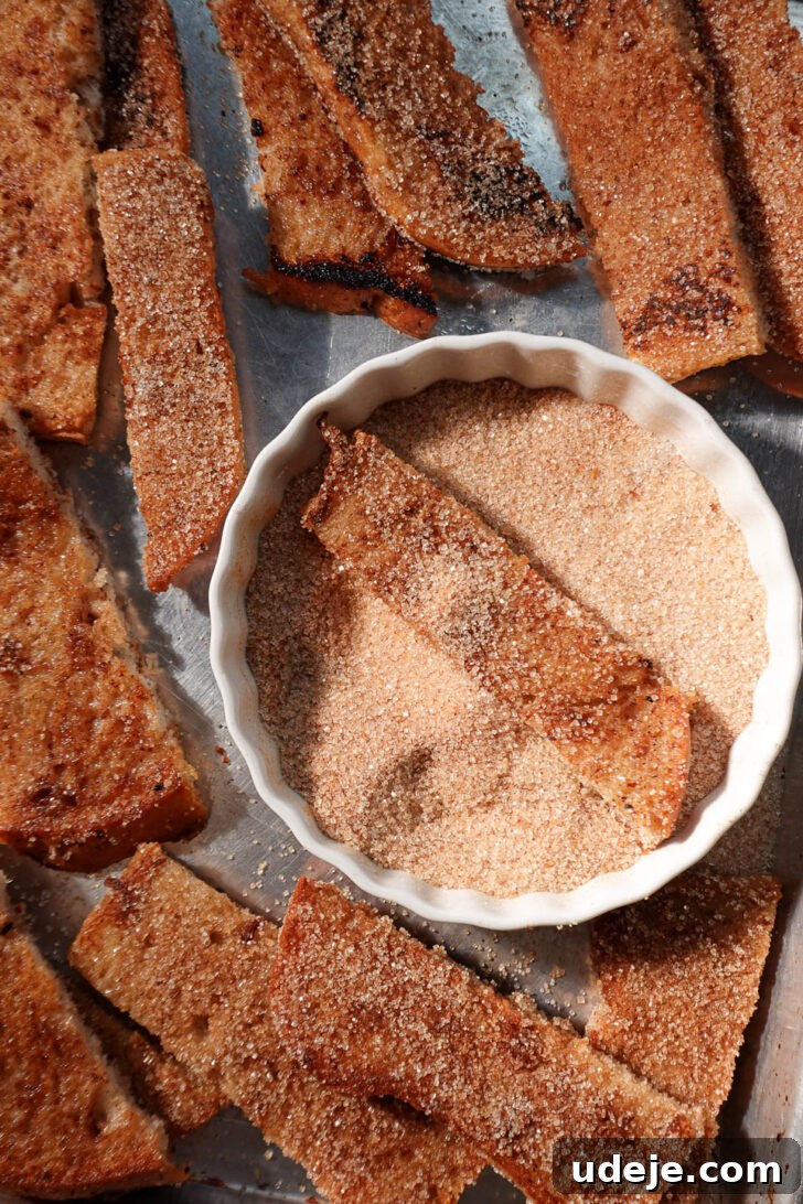 Spiced Vegan Gingerbread French Toast 5 Warm French toast sticks being rolled in a cinnamon and coconut sugar mixture on a plate, showing the glistening coating