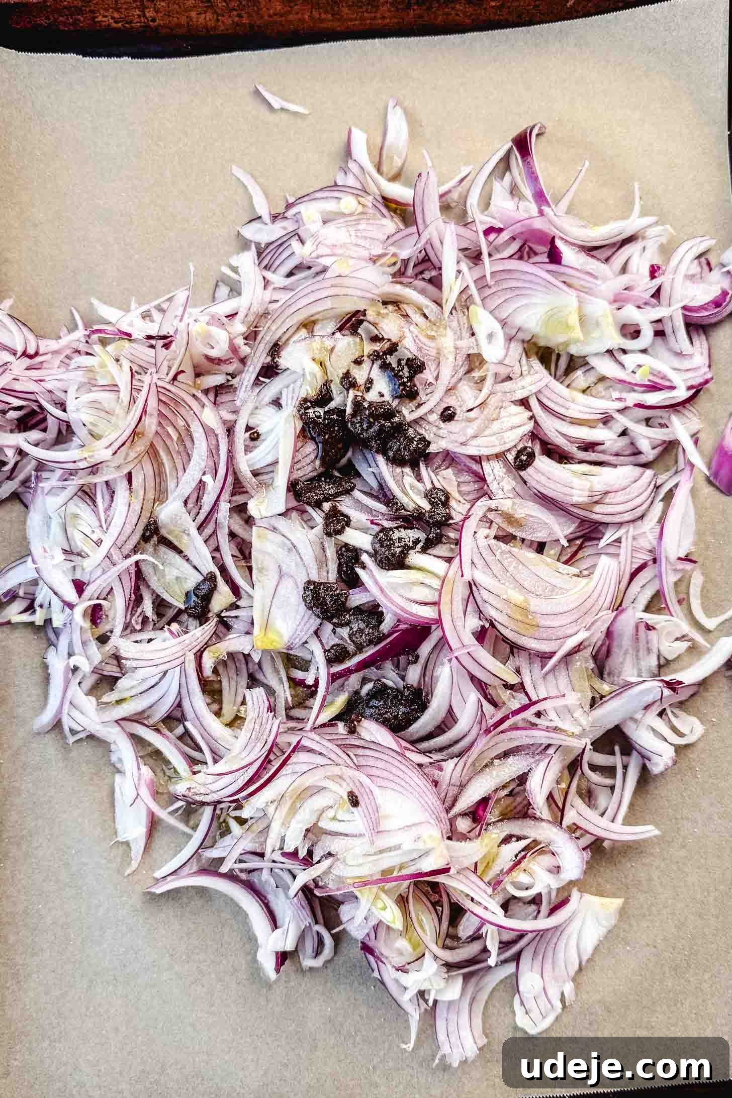 One-Pan Zesty Sumac Chicken and Onions 4 Thinly sliced red onions are spread on a parchment-lined sheet pan, with dollops of seasoned oil paste drizzled over them, ready to be tossed.