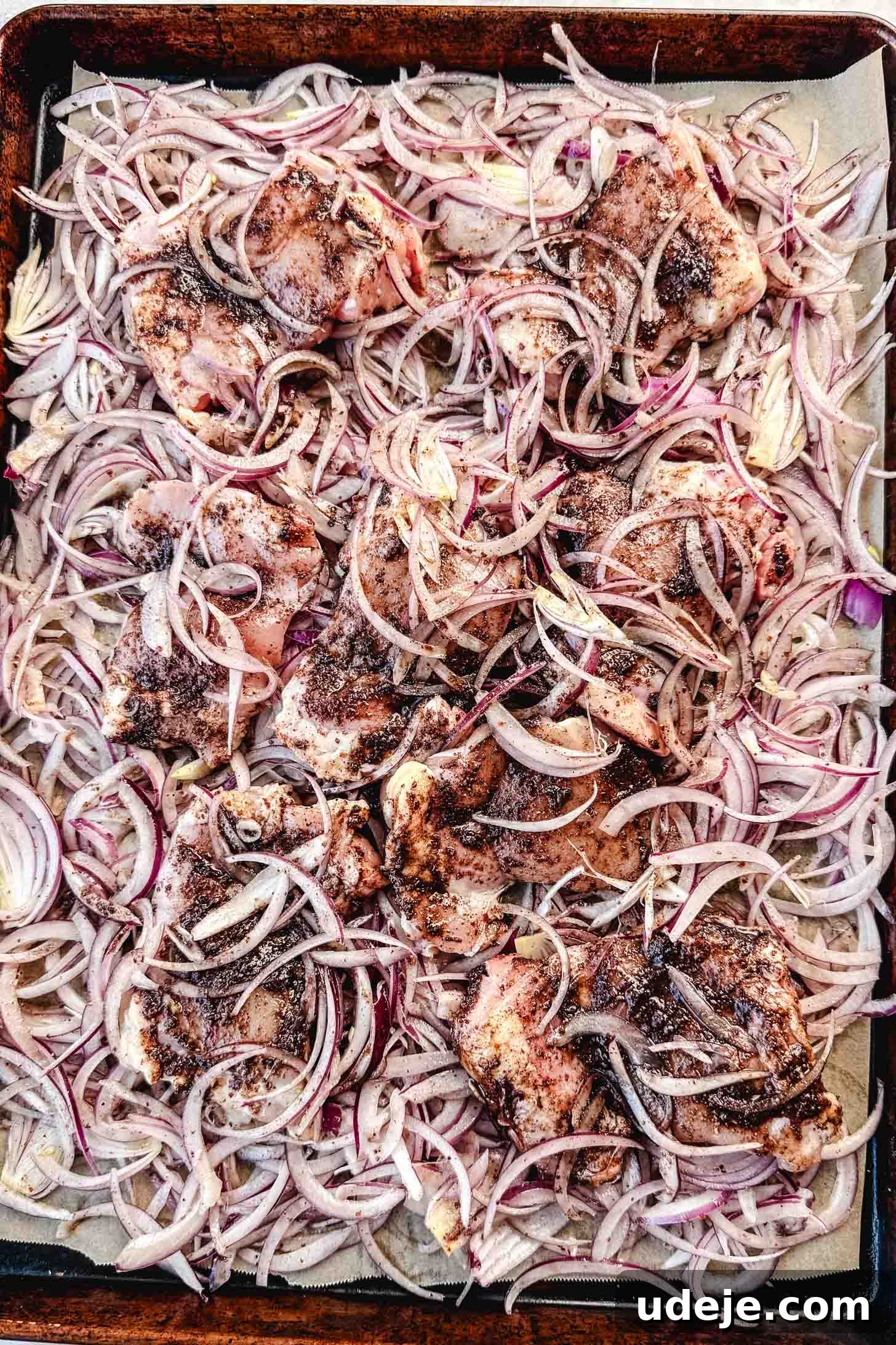 One-Pan Zesty Sumac Chicken and Onions 6 Raw chicken thighs and thinly sliced red onions are well seasoned with a rich spice and olive oil paste, spread evenly on a parchment-lined sheet pan, ready for baking.