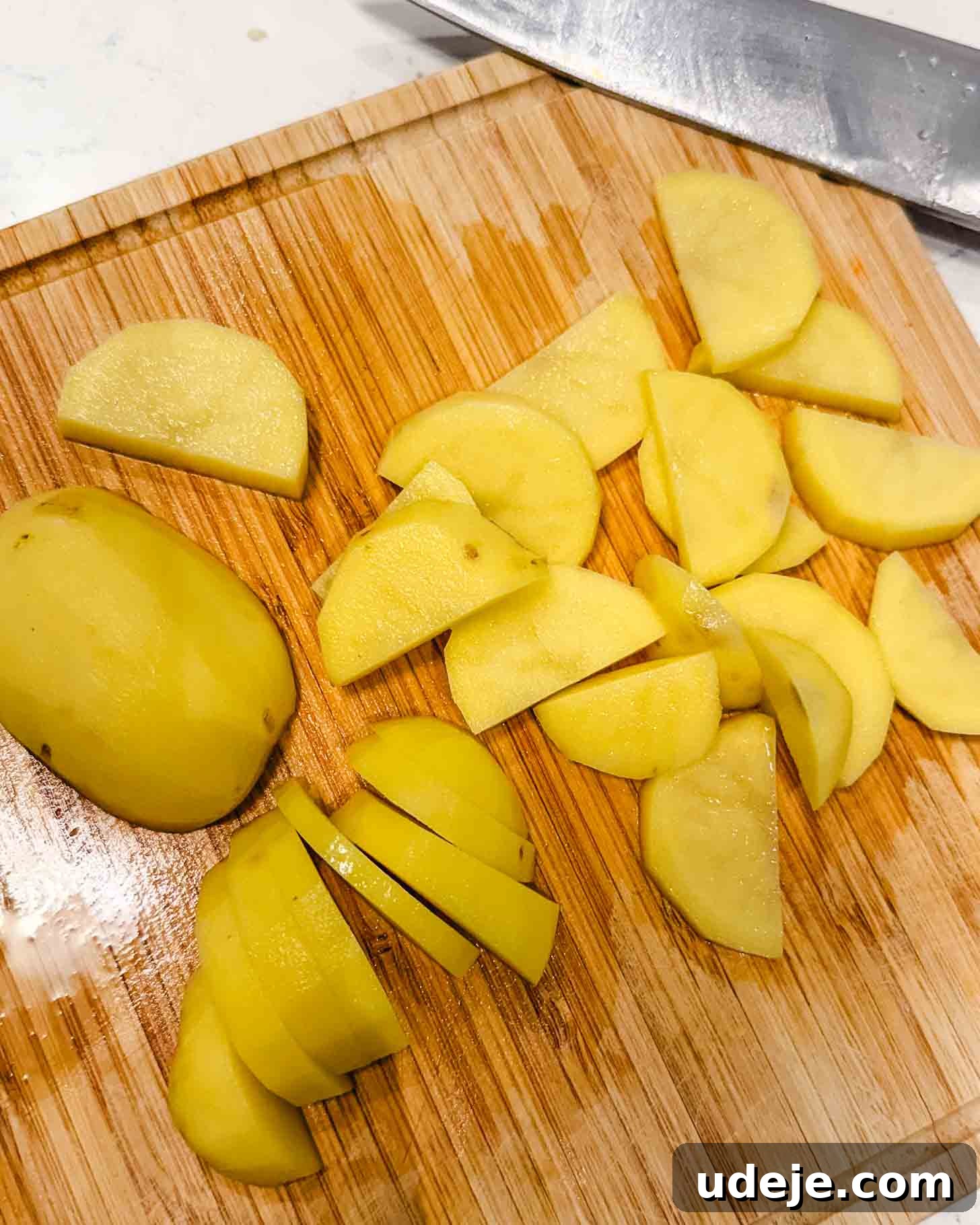 Hearty One-Pot Kofta and Potato Stew 5 Sliced yellow potatoes are arranged on a wooden cutting board with a large chef's knife nearby. Some potatoes are whole, while others are uniformly cut into thin, semi-circular slices, highlighting the precise preparation.