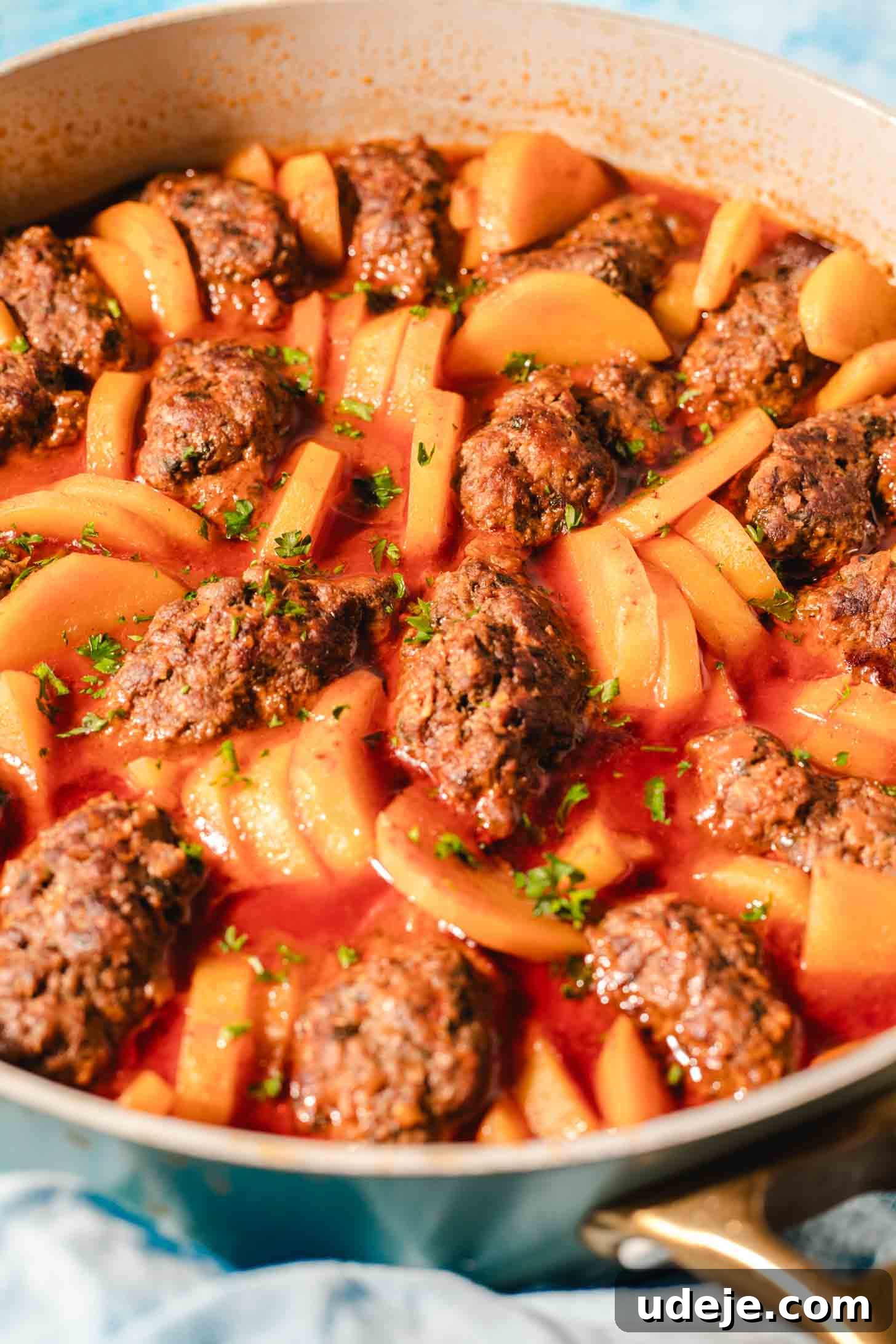 Hearty One-Pot Kofta and Potato Stew 9 A pan filled with perfectly cooked, oval-shaped meatballs and tender sliced potatoes, bathed in a rich, vibrant tomato sauce. The dish is beautifully garnished with chopped fresh herbs, inviting a warm and satisfying meal.