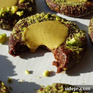 Close-up of a no-bake pistachio thumbprint cookie showing the chocolate base and pistachio filling dripping out