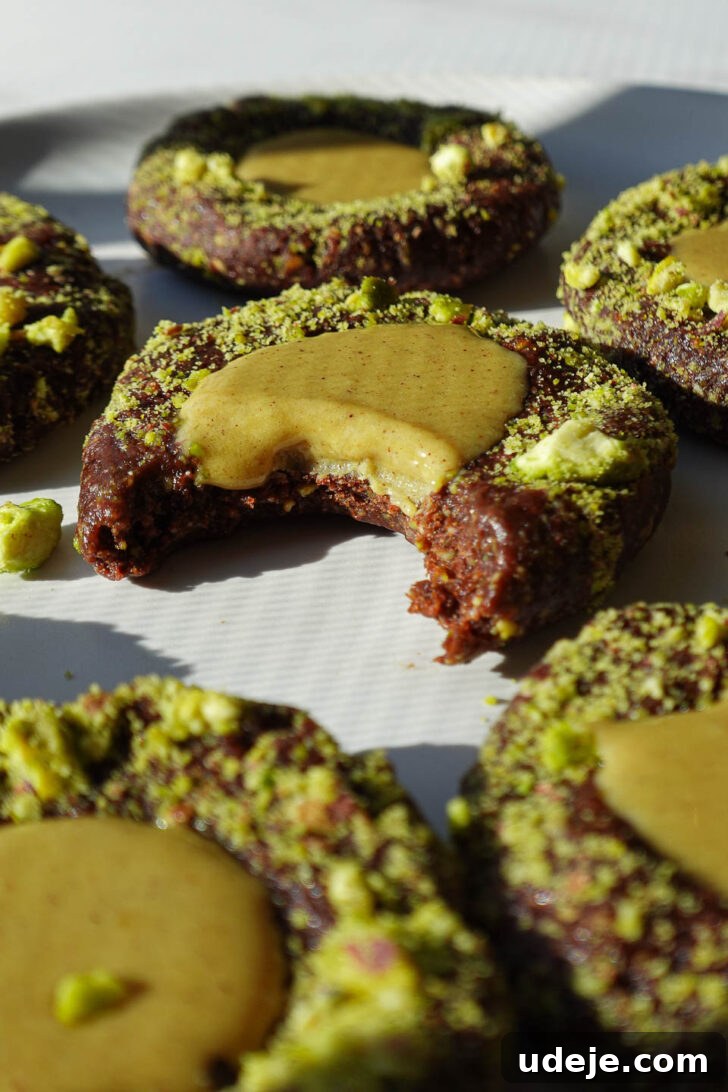 Effortless Vegan Gluten Free Pistachio Thumbprint Treats 6 Close-up of a no-bake pistachio thumbprint cookie showing the chocolate base and pistachio filling dripping out