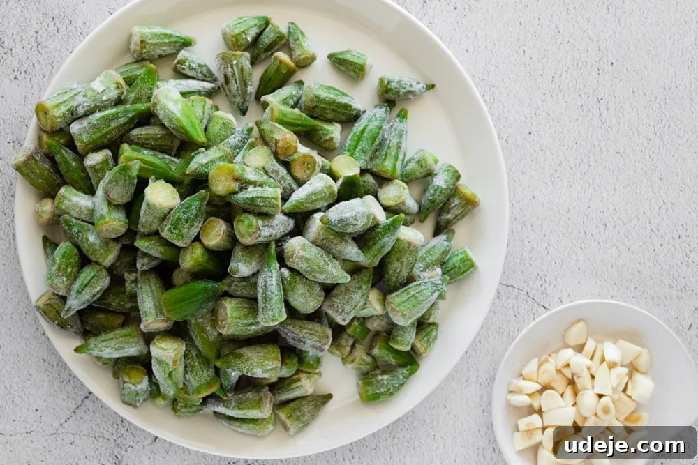 Flavorful Middle Eastern Bamya Okra Stew 8 A white plate holding frozen baby okra alongside a small bowl of roughly chopped garlic, illustrating prepared ingredients for the stew.