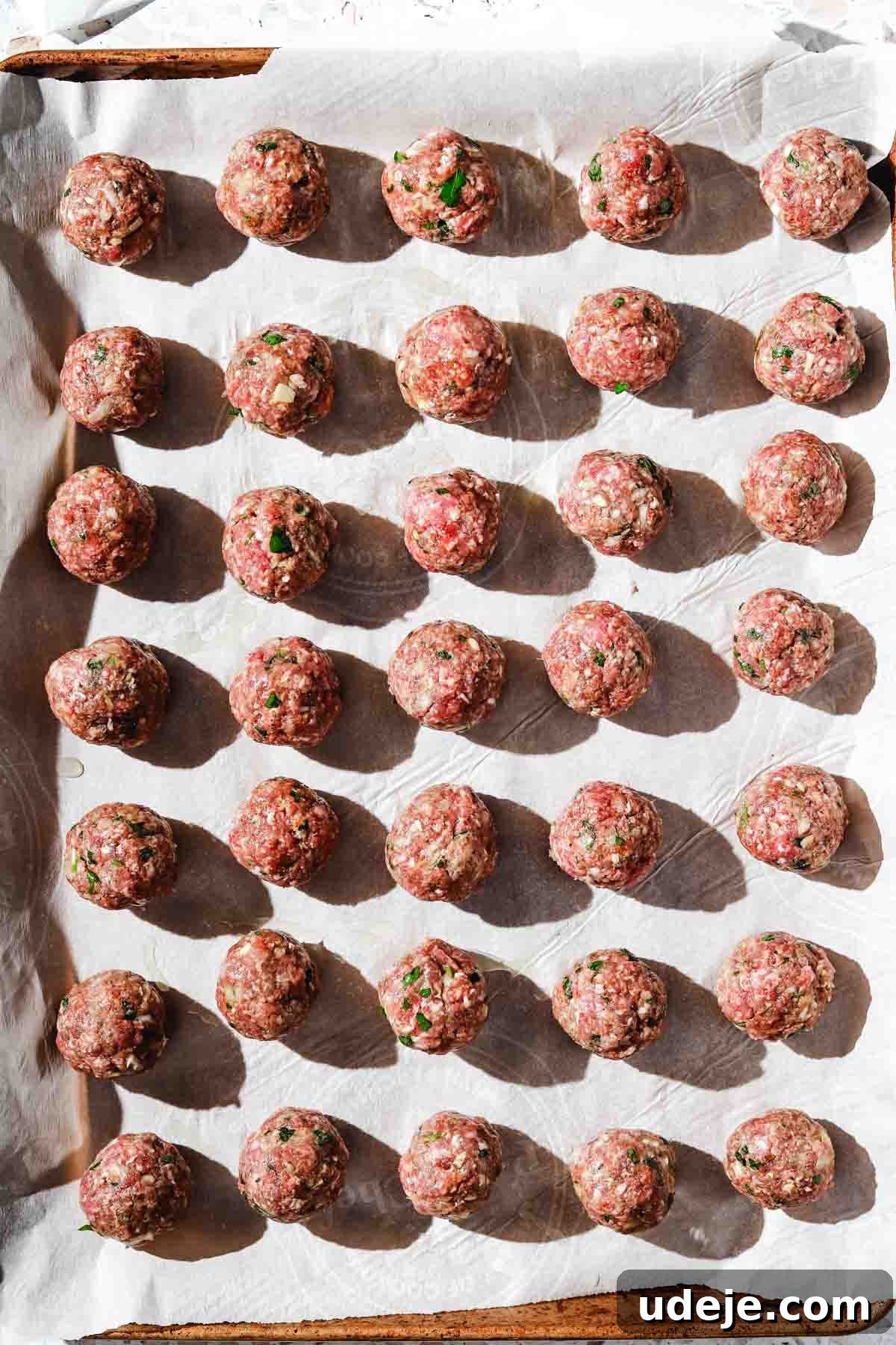 Kofta-Style Meatball Orzo Broth 5 A collection of perfectly shaped ground beef kofta meatballs, ready for cooking, arranged neatly on a large baking sheet lined with parchment paper.