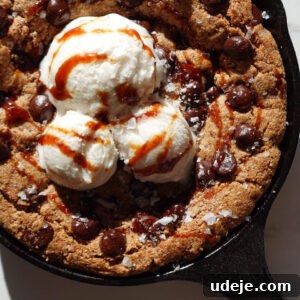 Delicious vegan and gluten-free chocolate chip skillet cookie dessert served warm straight from the skillet with vanilla ice cream on top, ready to be enjoyed.