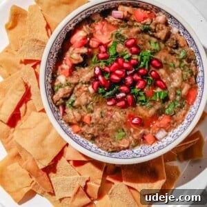 Charred Eggplant Baba Ghanoush 13 Baba ganoush with pomegranate and parsley on top in a white and blue patterend bowl on a large white plate surrounded with pita chips on a light marble background