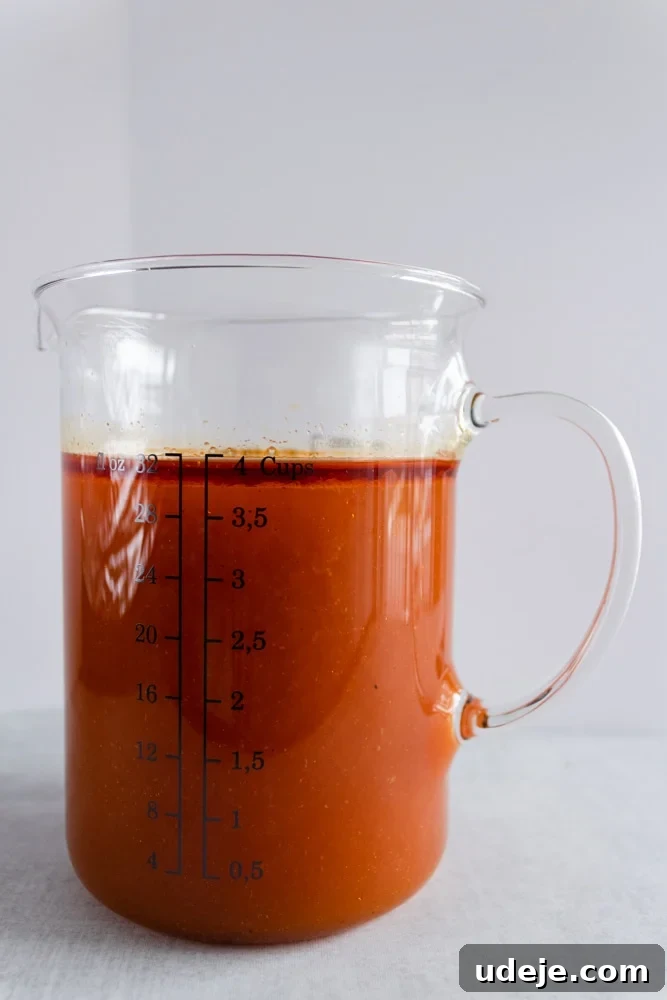 The Perfect Upside-Down Lamb Maqluba (Makloubeh) 8 Deep orange-red broth in a clear measuring cup, showing the rich color of the spiced stock with tomato paste.