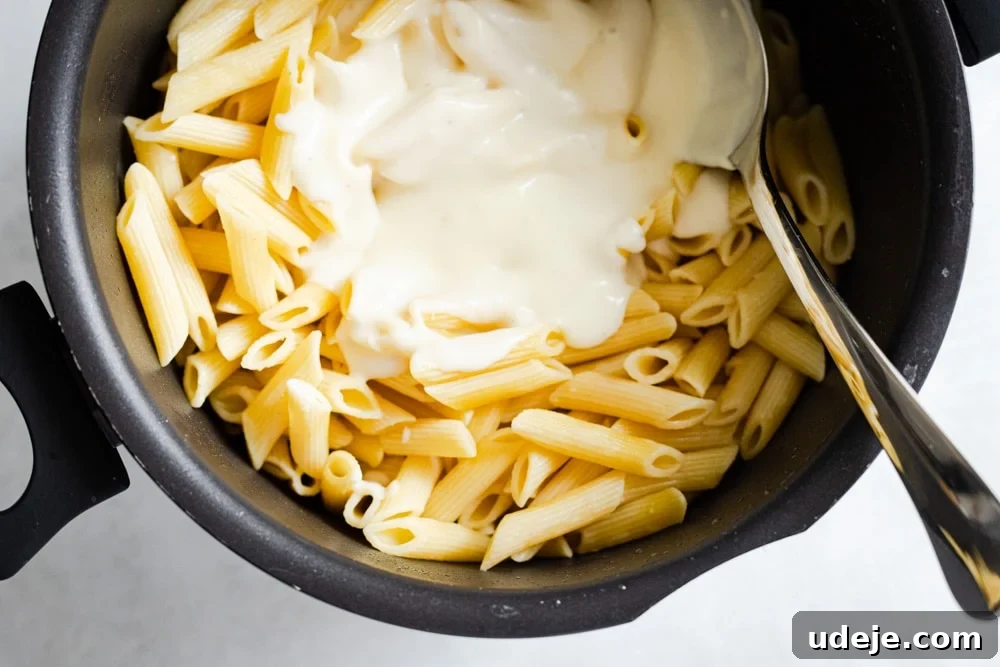 Creamy Bechamel Macaroni Bake 6 Cooked penne pasta being gently mixed with creamy Bechamel sauce in a large pot, ensuring every strand is coated.