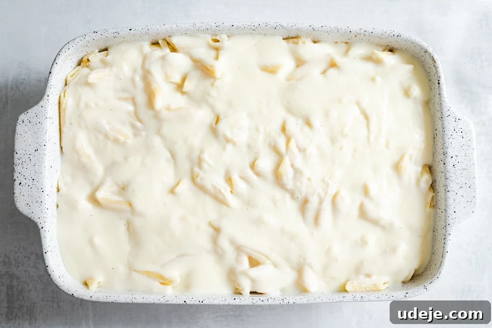 Creamy Bechamel Macaroni Bake 7 An unbaked casserole dish with layers of pasta, meat sauce, and a generous topping of creamy Bechamel, ready for the oven.