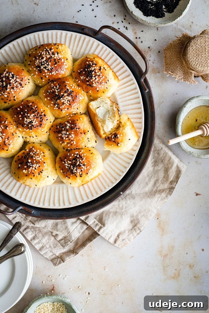 Cheesy Honeycomb Pull-Apart Bread 2 A beautifully arranged plate of golden Honeycomb Bread, with one roll cut in half to show the melted cream cheese filling. Small dishes of honey, sesame seeds, and nigella seeds are artfully placed around it.