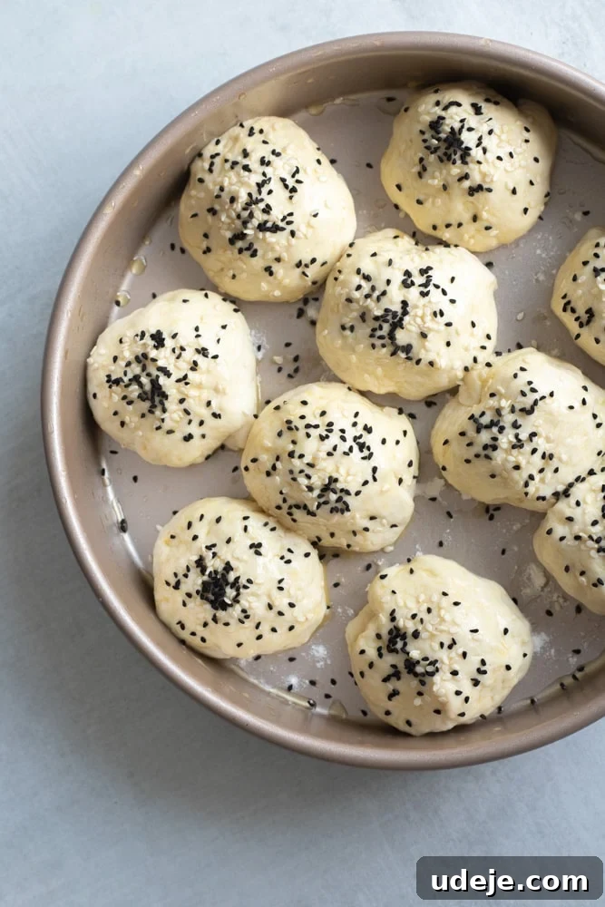 Cheesy Honeycomb Pull-Apart Bread 5 Unbaked Honeycomb Bread dough balls, neatly arranged in a baking pan, generously sprinkled with sesame seeds and nigella seeds, showcasing their readiness for baking.