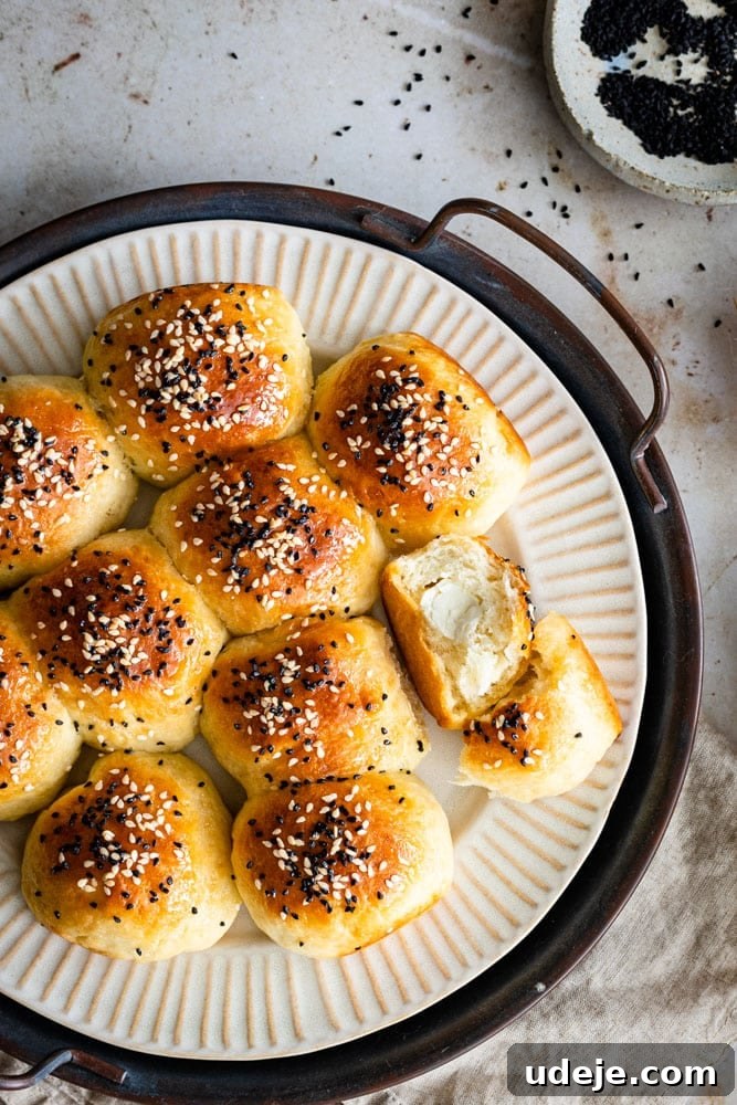 Cheesy Honeycomb Pull-Apart Bread 7 A rustic plate laden with golden, perfectly rounded Honeycomb Bread rolls, generously topped with black sesame and nigella seeds. One roll is gently pulled apart, revealing its soft, creamy cheese filling. A small bowl of extra seeds rests nearby, completing the inviting scene.