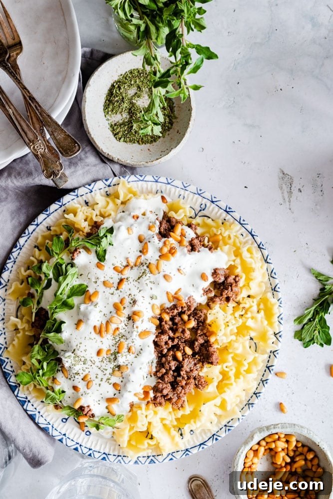 Quick Arabic Pasta with Zesty Yogurt Sauce 2 A vibrant plate of Arabic pasta, garnished generously with golden toasted pine nuts and fresh mint, ready to be enjoyed. The creamy yogurt sauce and spiced ground beef are clearly visible, promising a delicious meal.