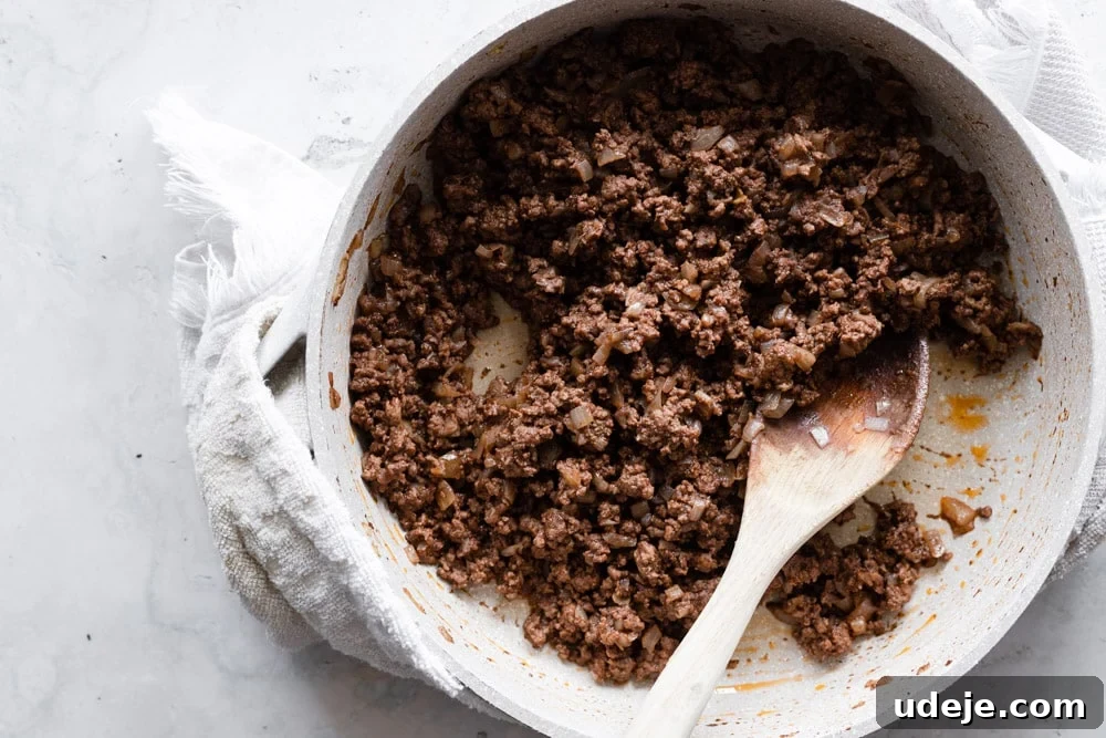Quick Arabic Pasta with Zesty Yogurt Sauce 4 A large skillet filled with perfectly cooked and spiced ground beef and sautéed onions, ready to be incorporated into the Arabic pasta dish. A wooden spoon rests in the pan, highlighting the rich texture of the beef.