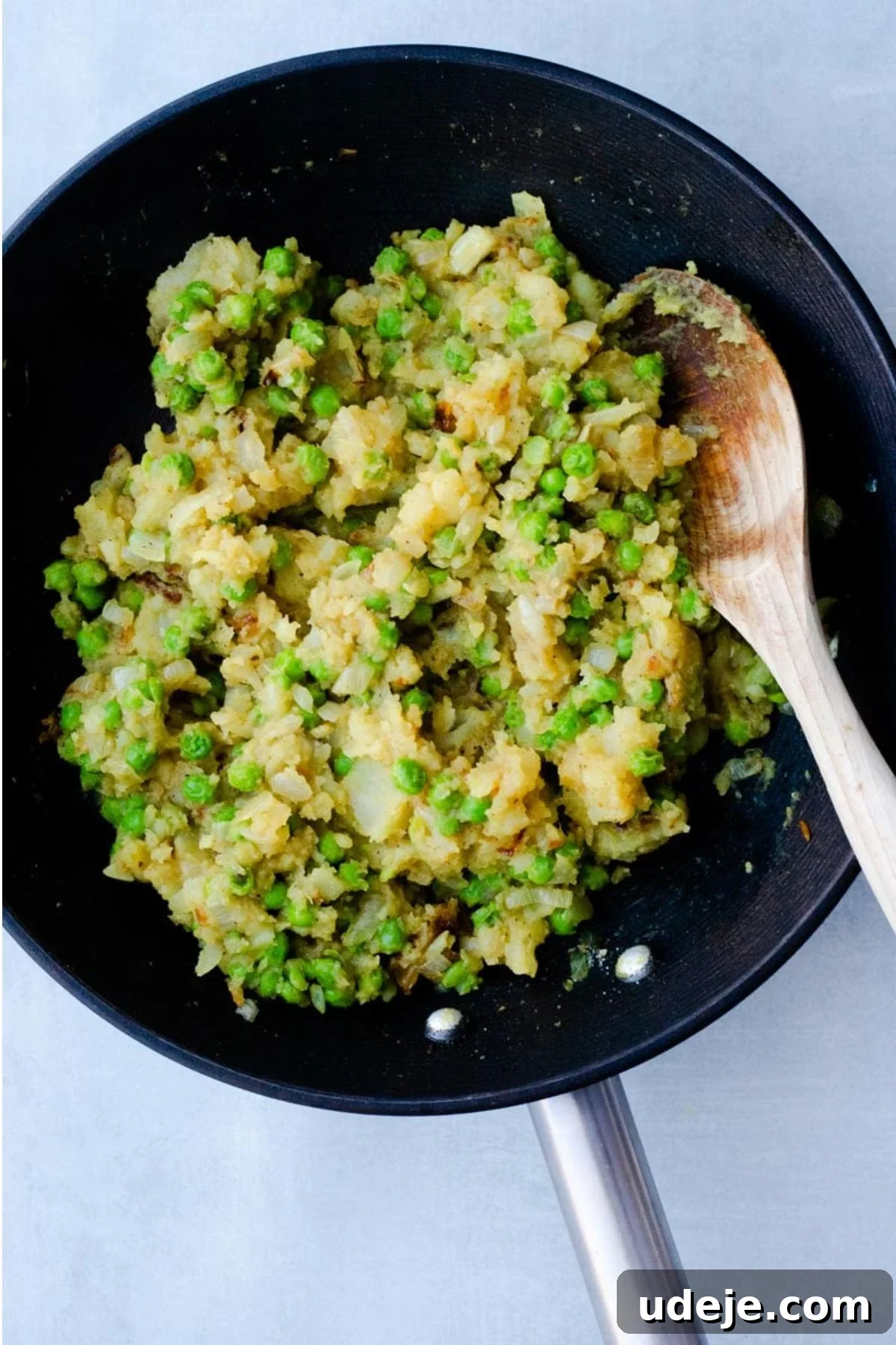 Your Guide to Authentic Homemade Sambousek 11 a mixture of mashed potatoes, onions, spices and peas in a black pan with a wooden spoon